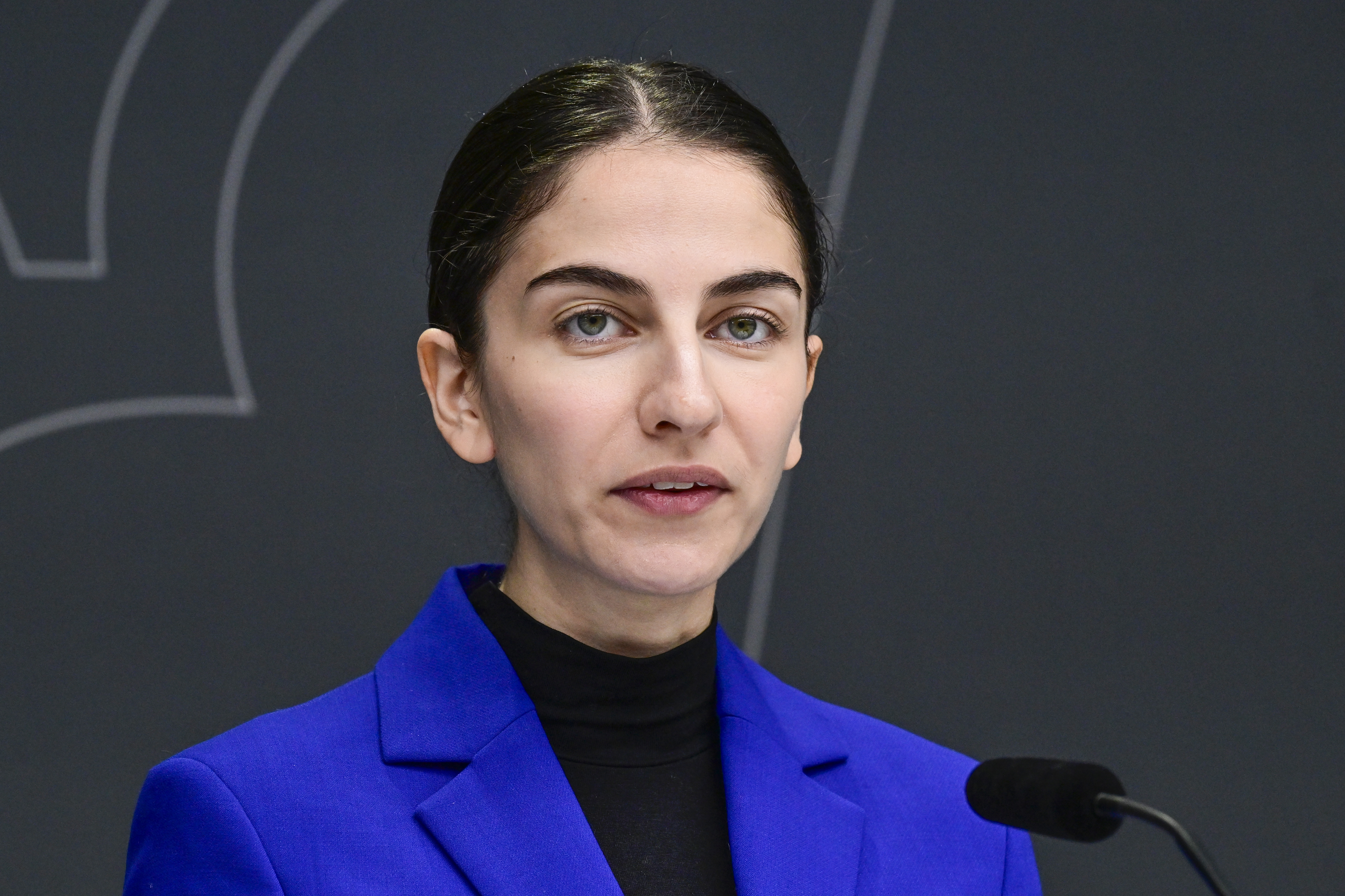 Klimat- och miljöminister Romina Pourmokhtari (L) med mörkt hår uppsatt, iförd blå kavaj och svart polotröja, står framför en mikrofon mot mörk bakgrund.