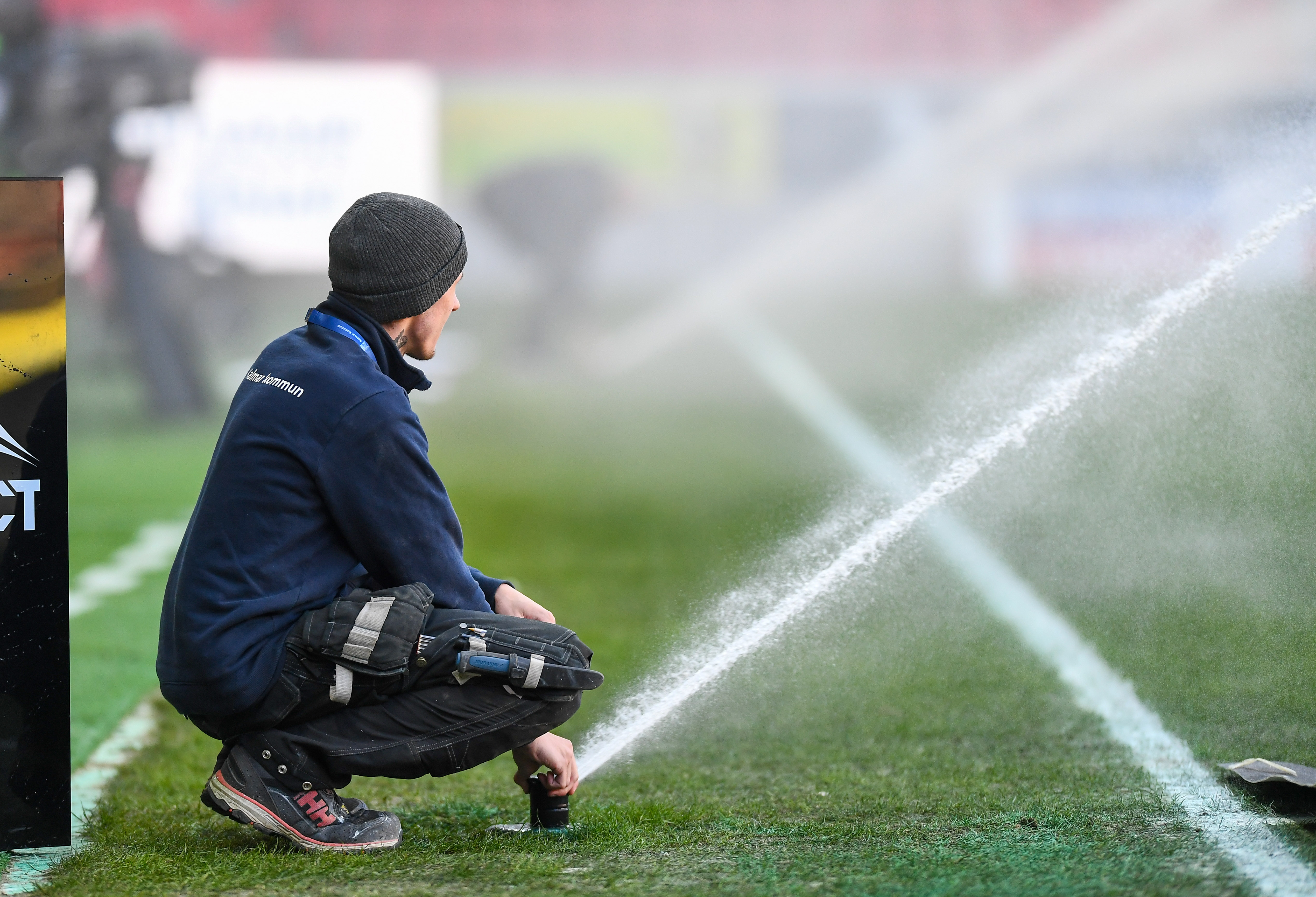 En vaktmästare justerar en sprinkler invid en fotbollsplan.