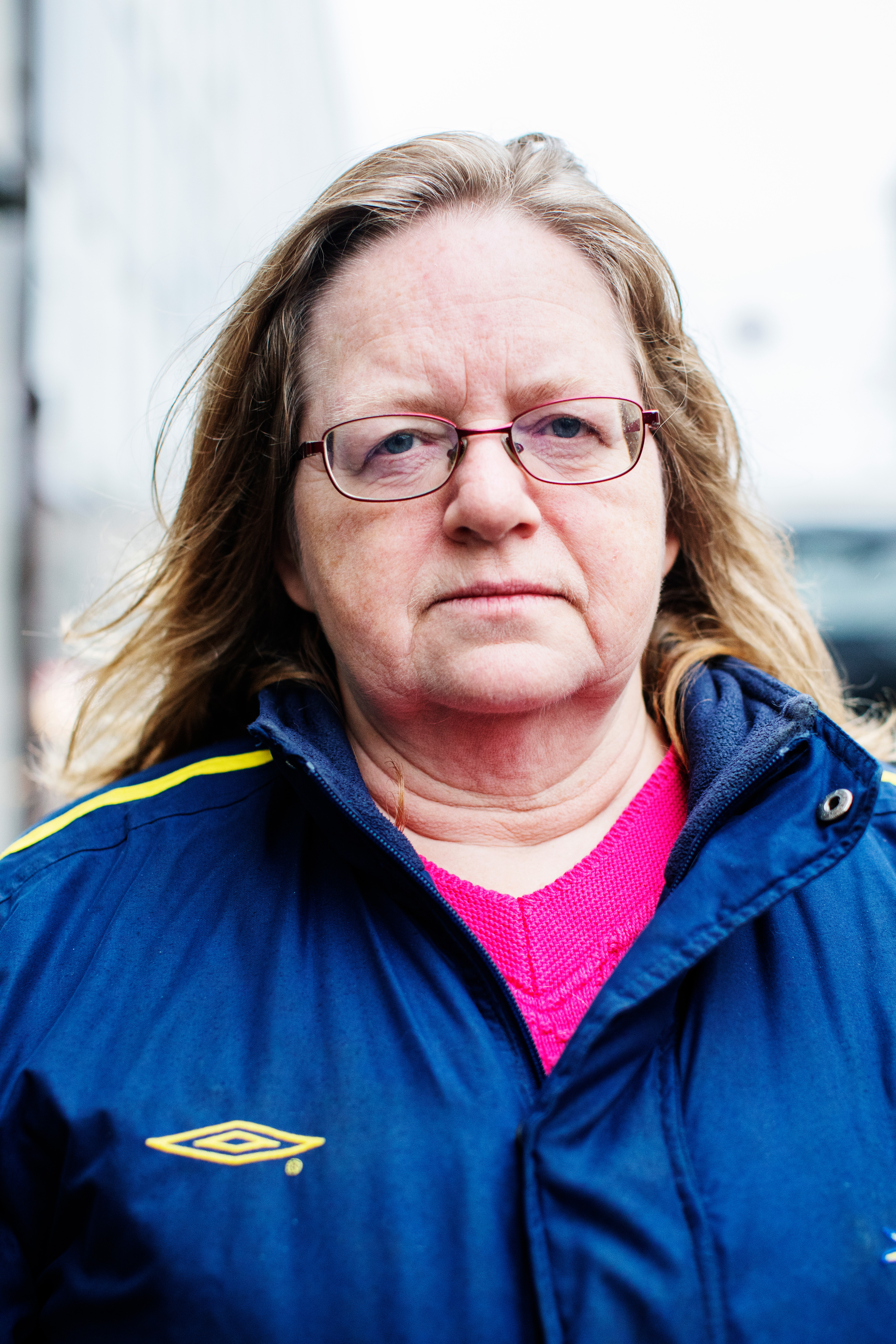 Carina Olsson med glasögon och långt hår står utomhus, har en blå sportjacka med gul logotyp över en rosa tröja och tittar in i kameran.