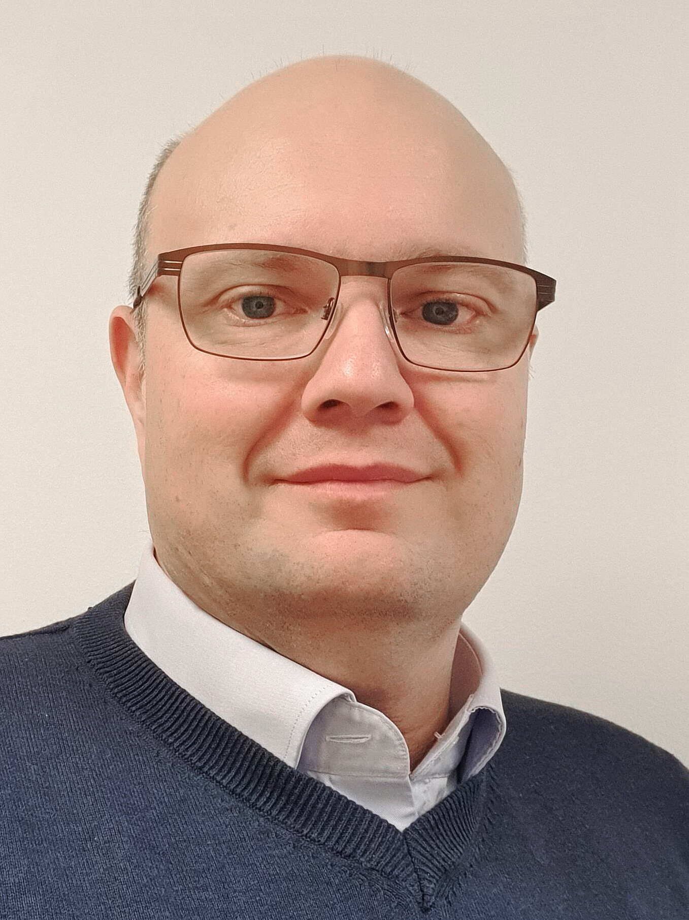 Jens Lindström med glasögon, rakat huvud och ljus hy har på sig en skjorta med krage och en mörk tröja. Han ser in i kameran.