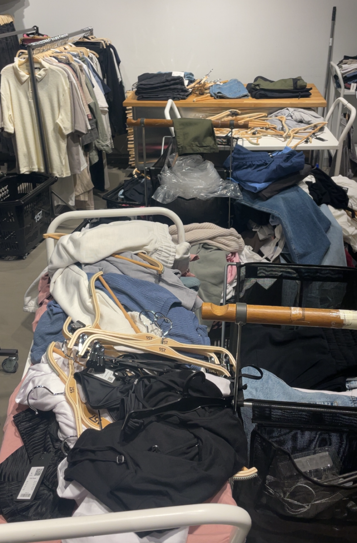 Klädställ och vagnar med kläder och galgar i en butiksmiljö.