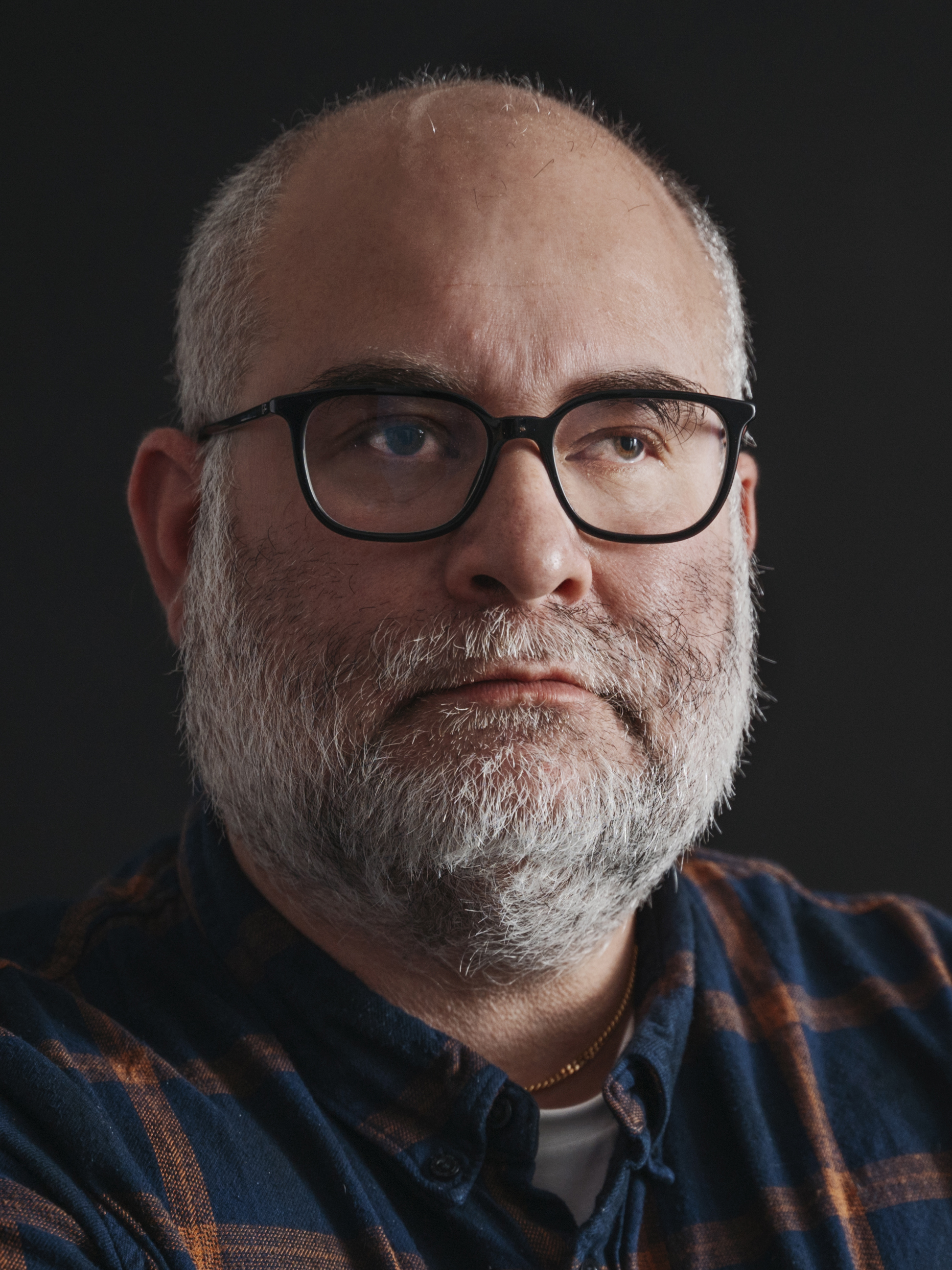 Daniel Andersson med skägg och glasögon, i rutig skjorta, tittar lite åt sidan mot en mörk bakgrund.
