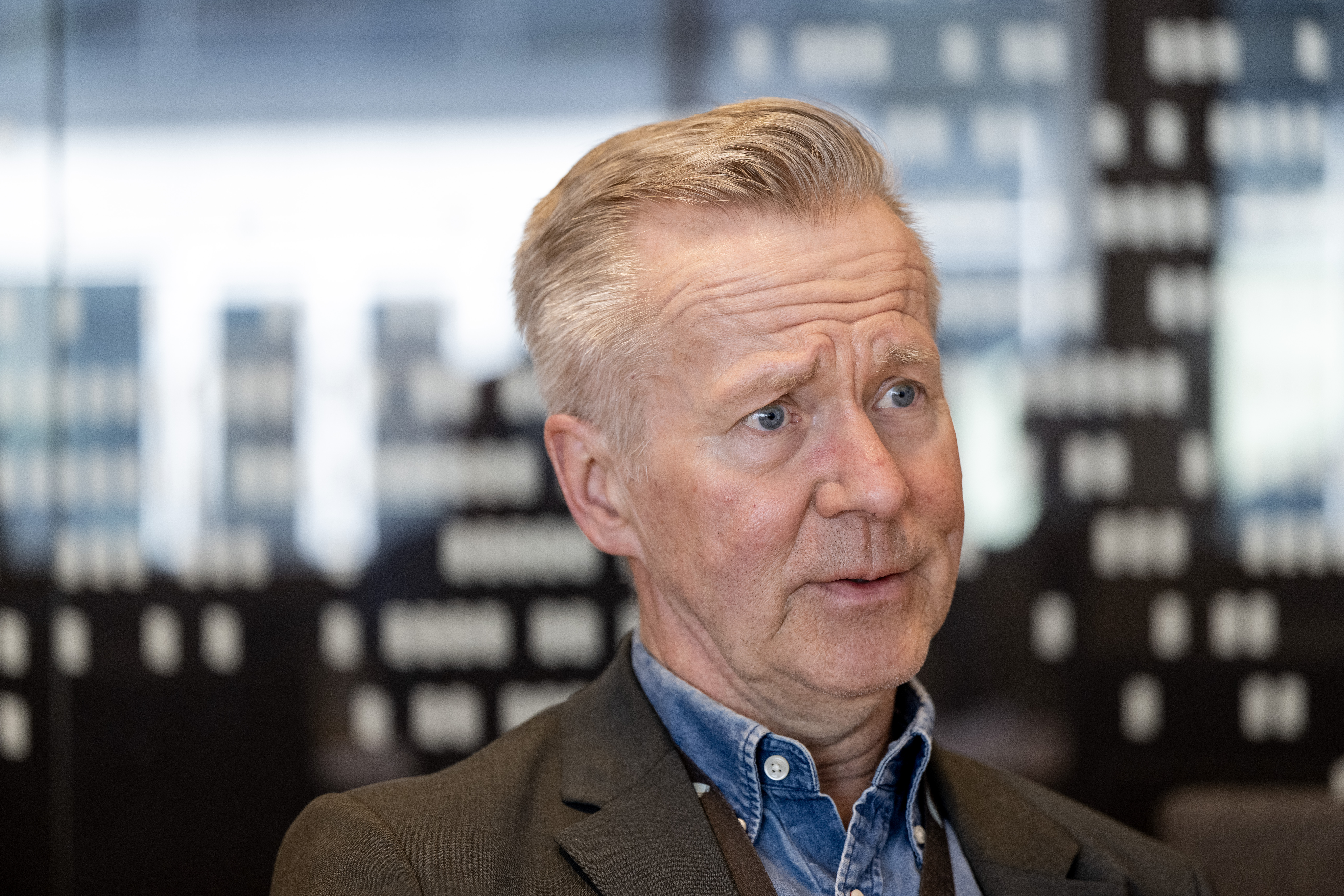 Mats Taaveniku med ljust hår och kavaj sitter inomhus och tittar åt sidan.