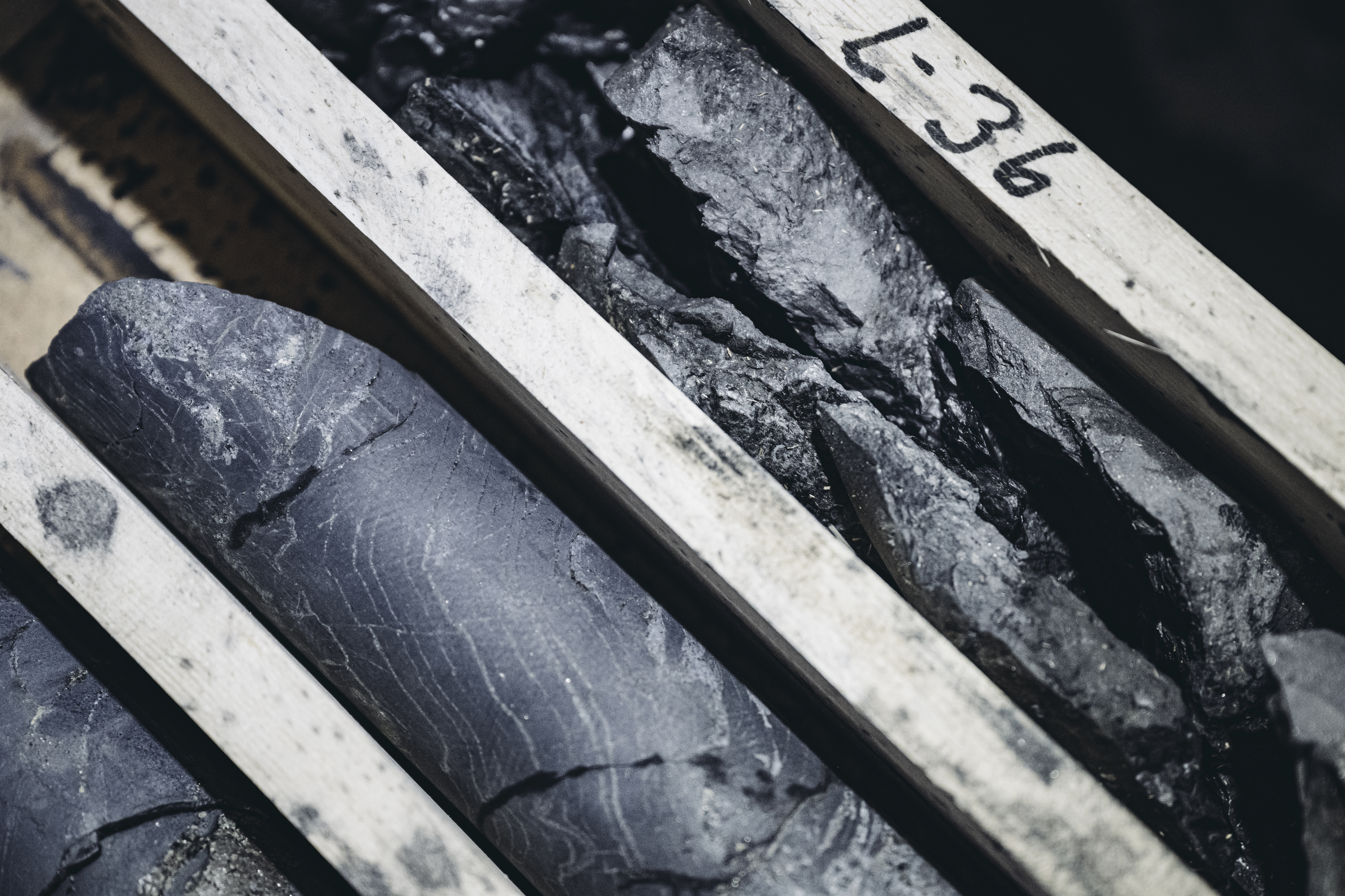 Närbild av borrkärnor placerade i en trälåda med etiketten "L-36", där materialets textur och skiktning syns.