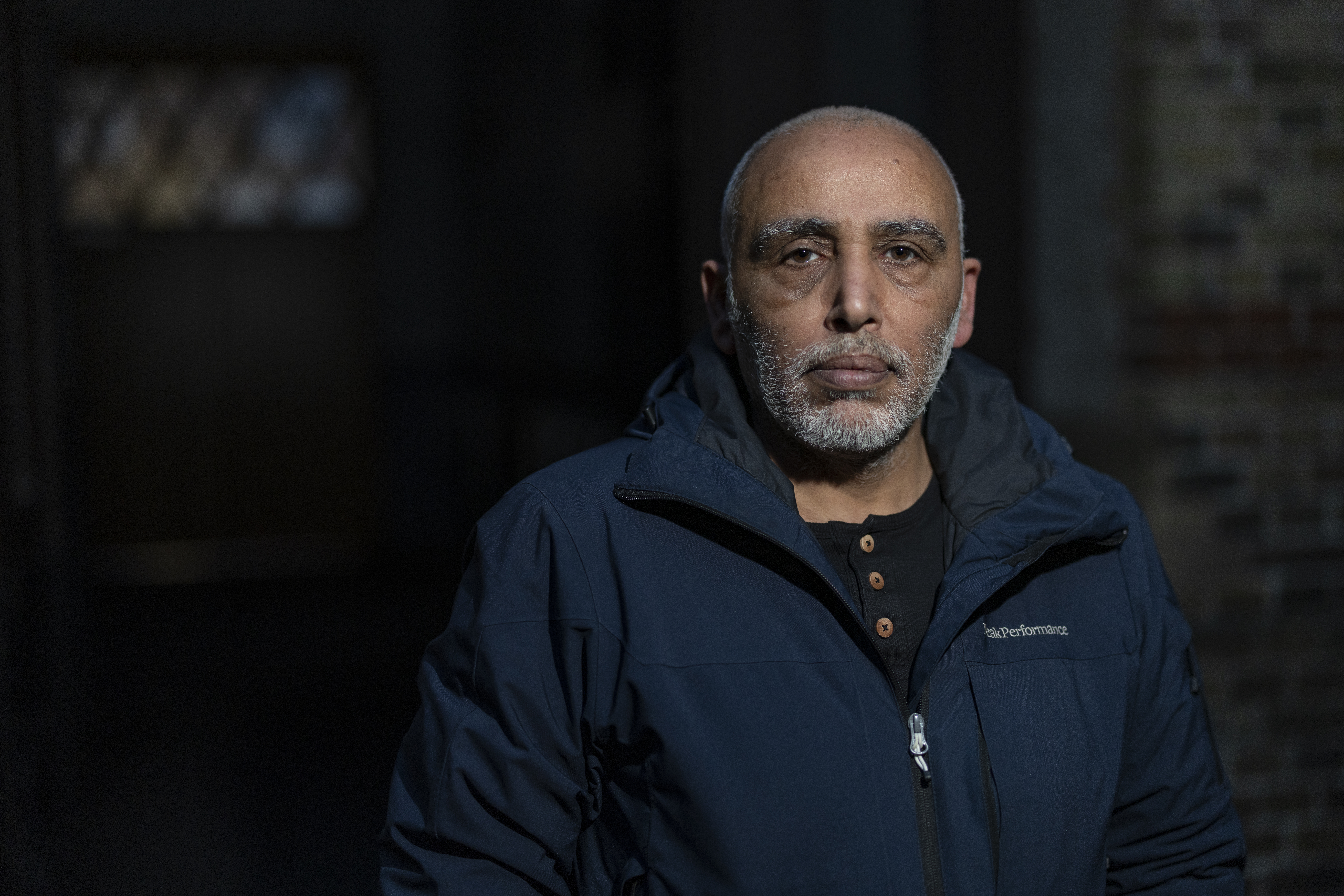 En medelålders man med gråsprängt skägg och kort hår står inomhus, har en mörkblå jacka och tittar rakt mot kameran.