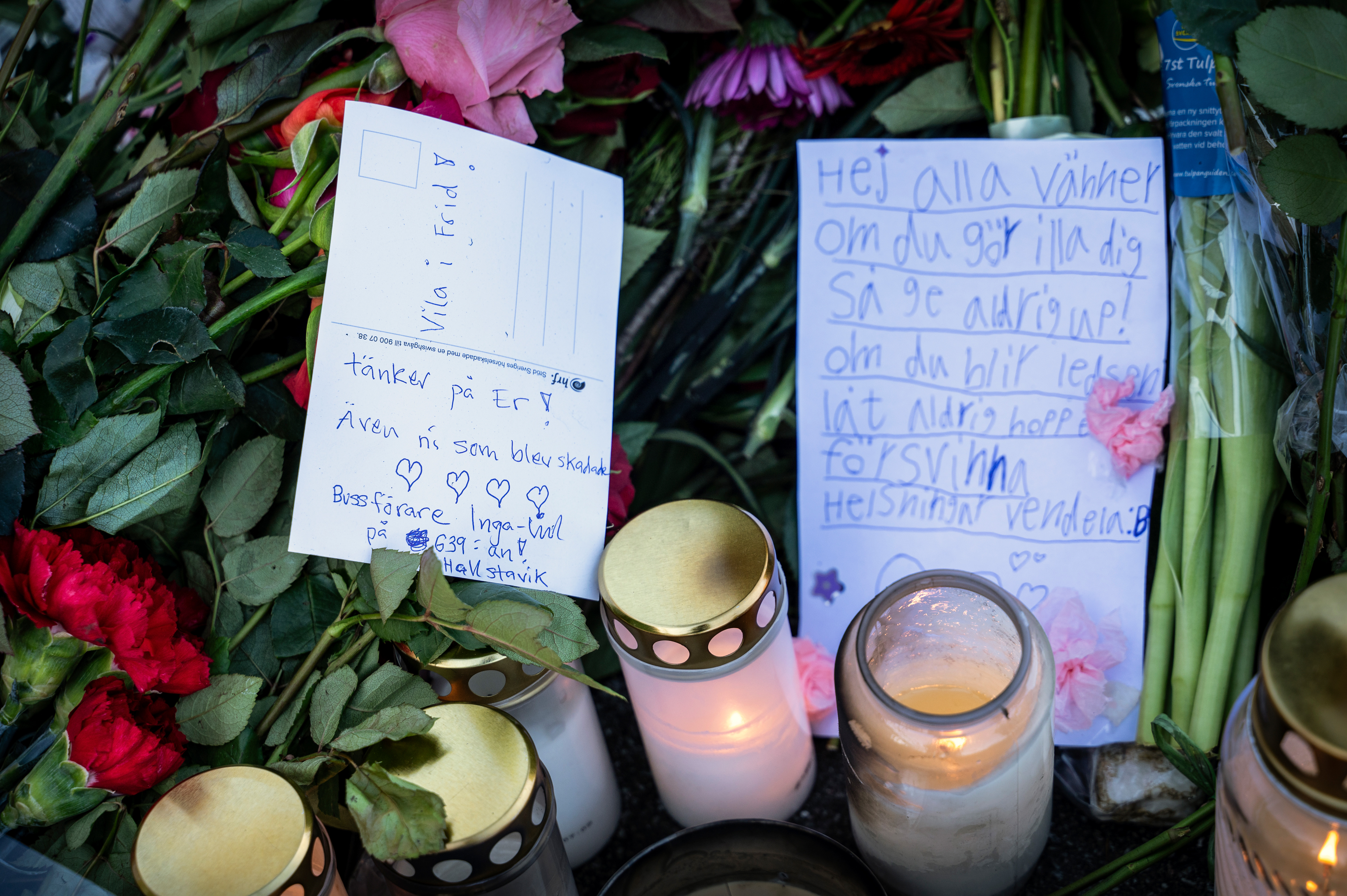 Blommor, handskrivna lappar och tända ljus på en minnesplats som visar deltagande och minne efter den dödliga bussolyckan i Stockholm.