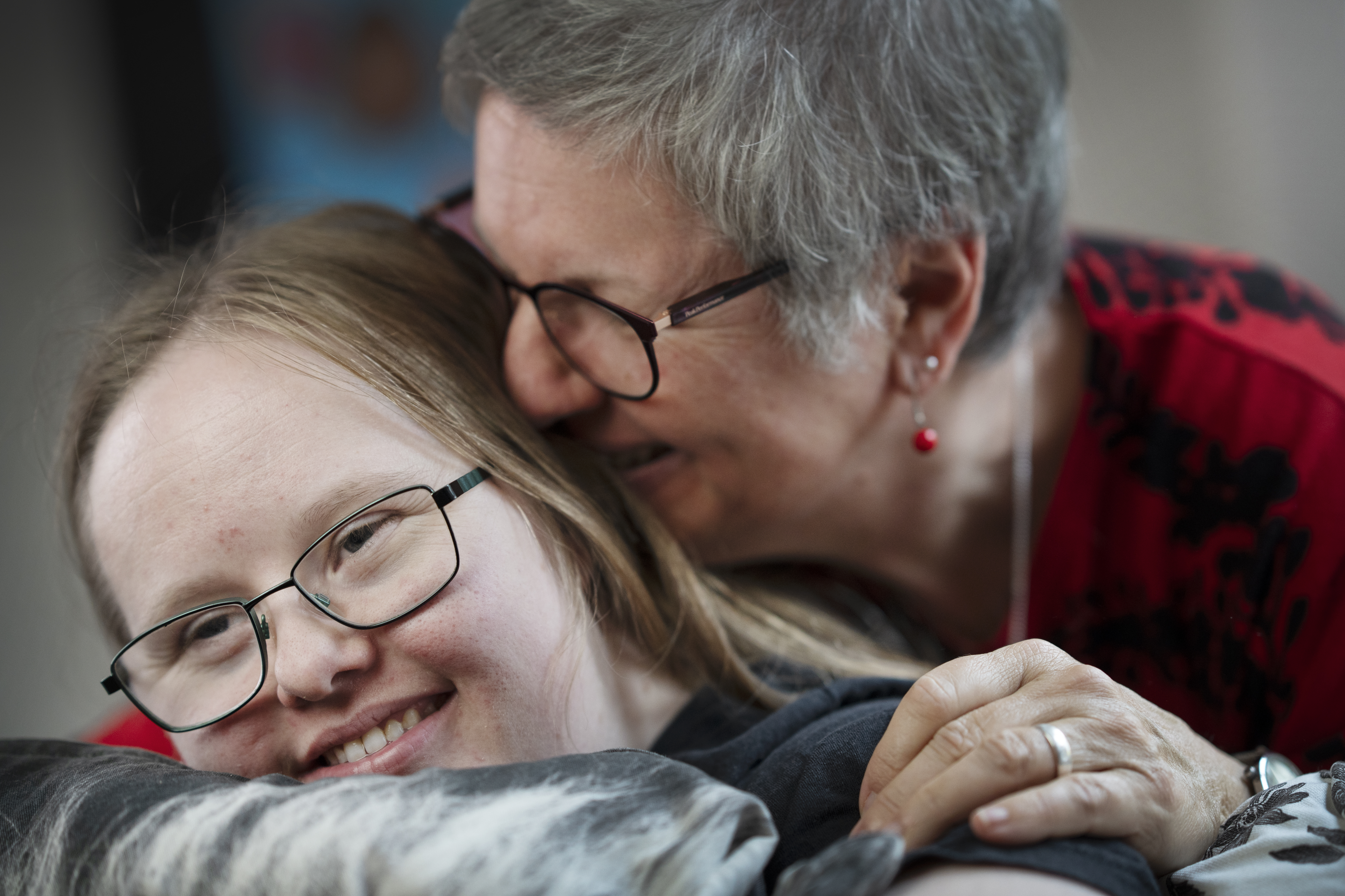 Marlise kramar Mia. Båda har glasögon och sitter nära varandra inomhus.