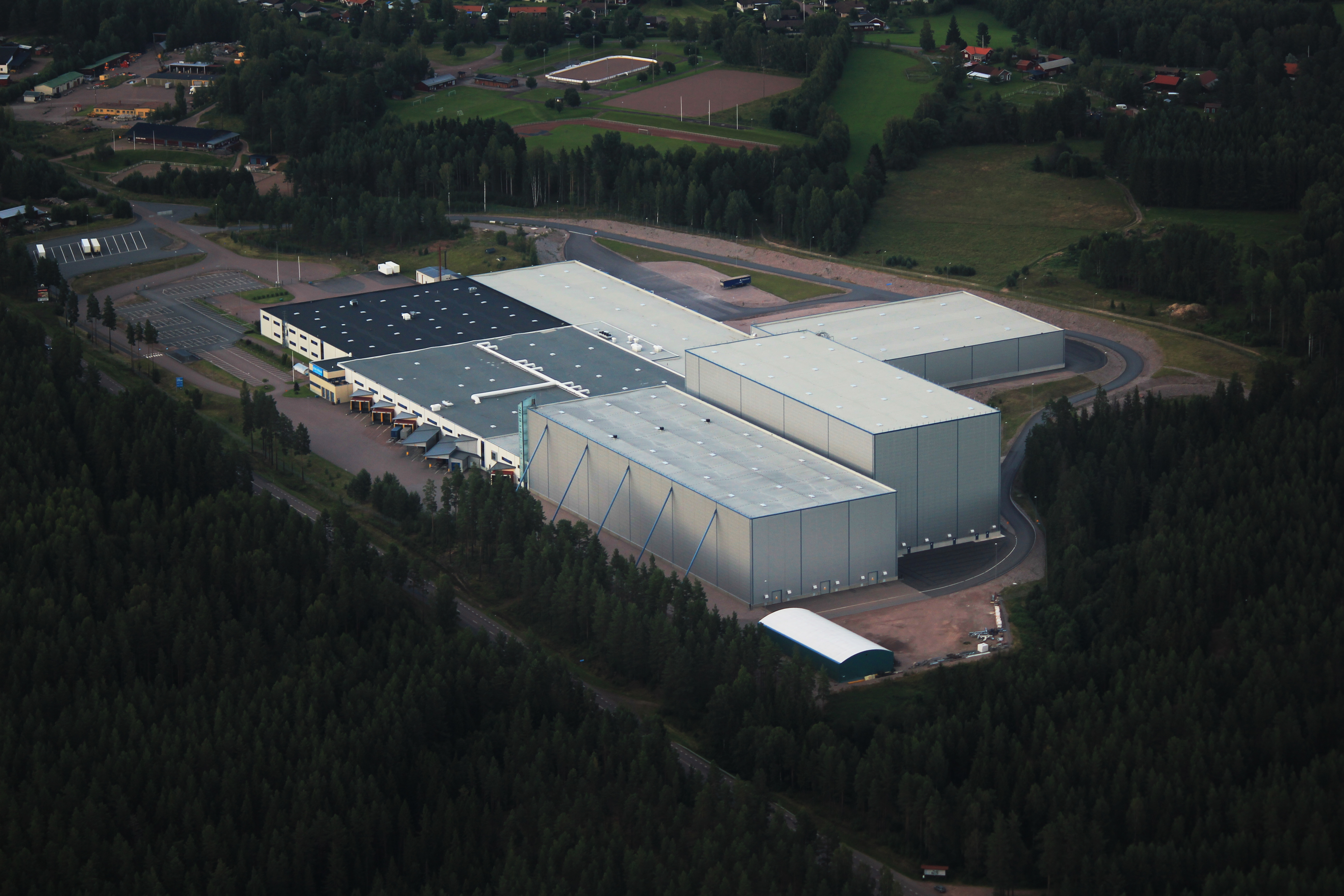 Flygfoto av Clas Ohlsons stor lagerbyggnad med lagerbyggnader, omgiven av skog, fält, vägar och parkeringsplatser.