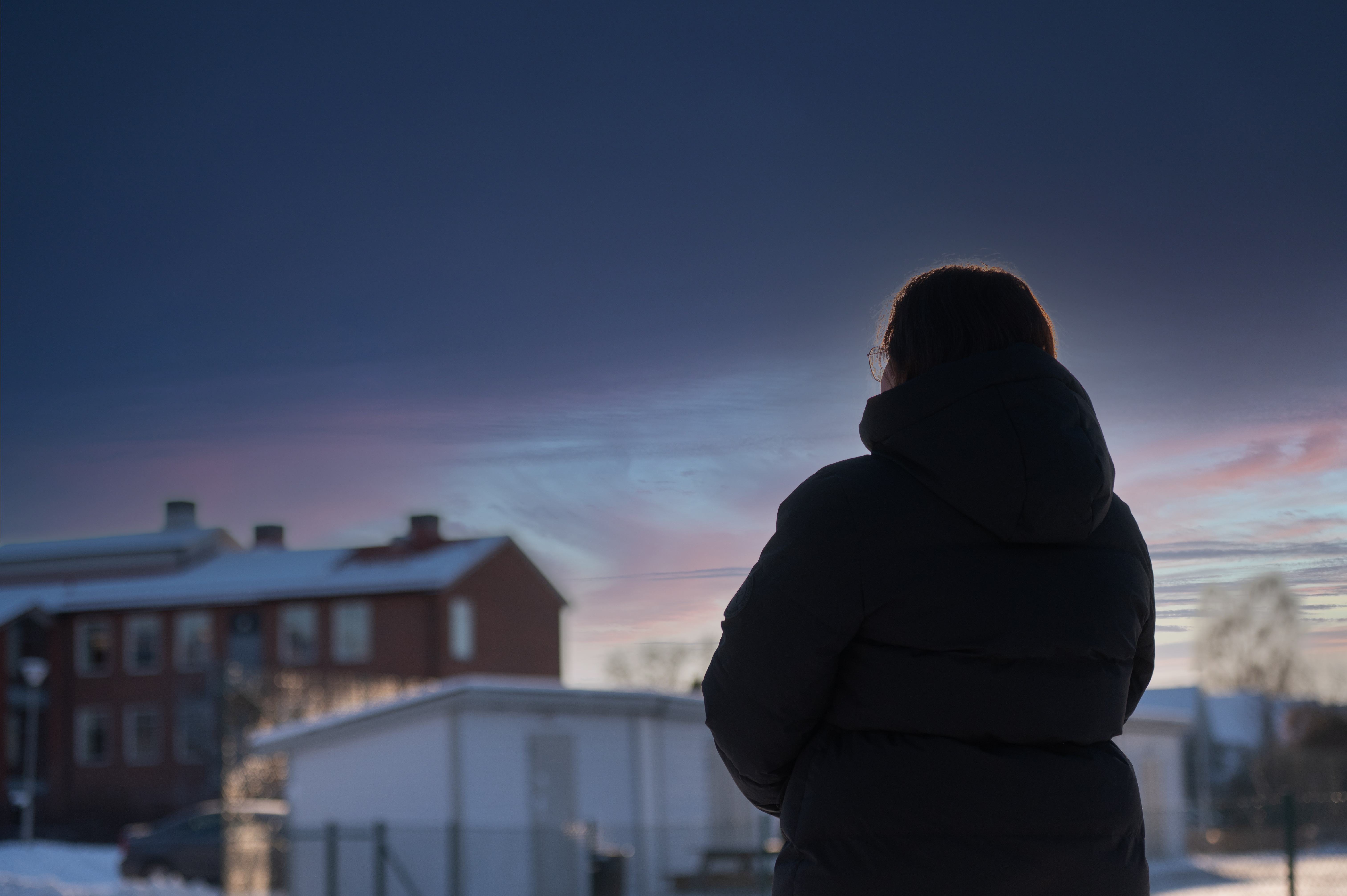 En person som bär en vinterjacka siluett mot bakgrunden av ett vinterbostadsområde.