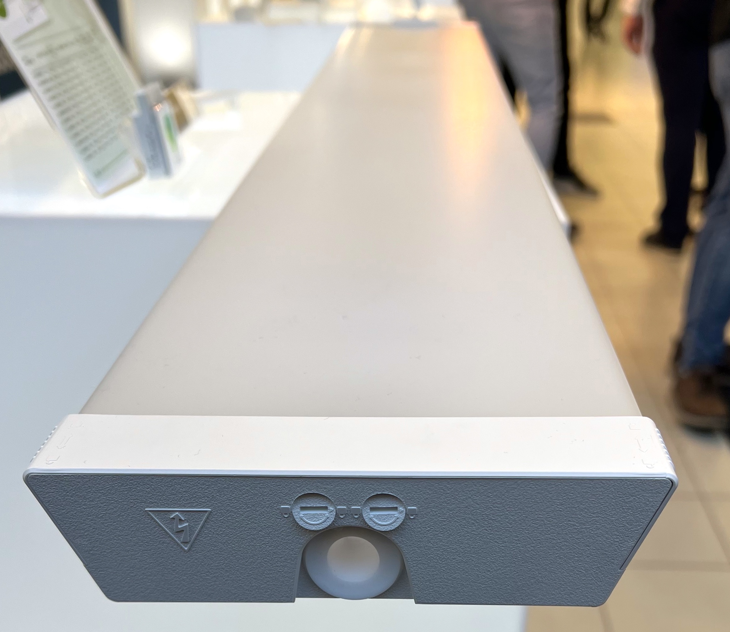 Närbild av änden av en rektangulär vit armatur med två runda fördjupningar och en varningssymbol i inomhusmiljö.