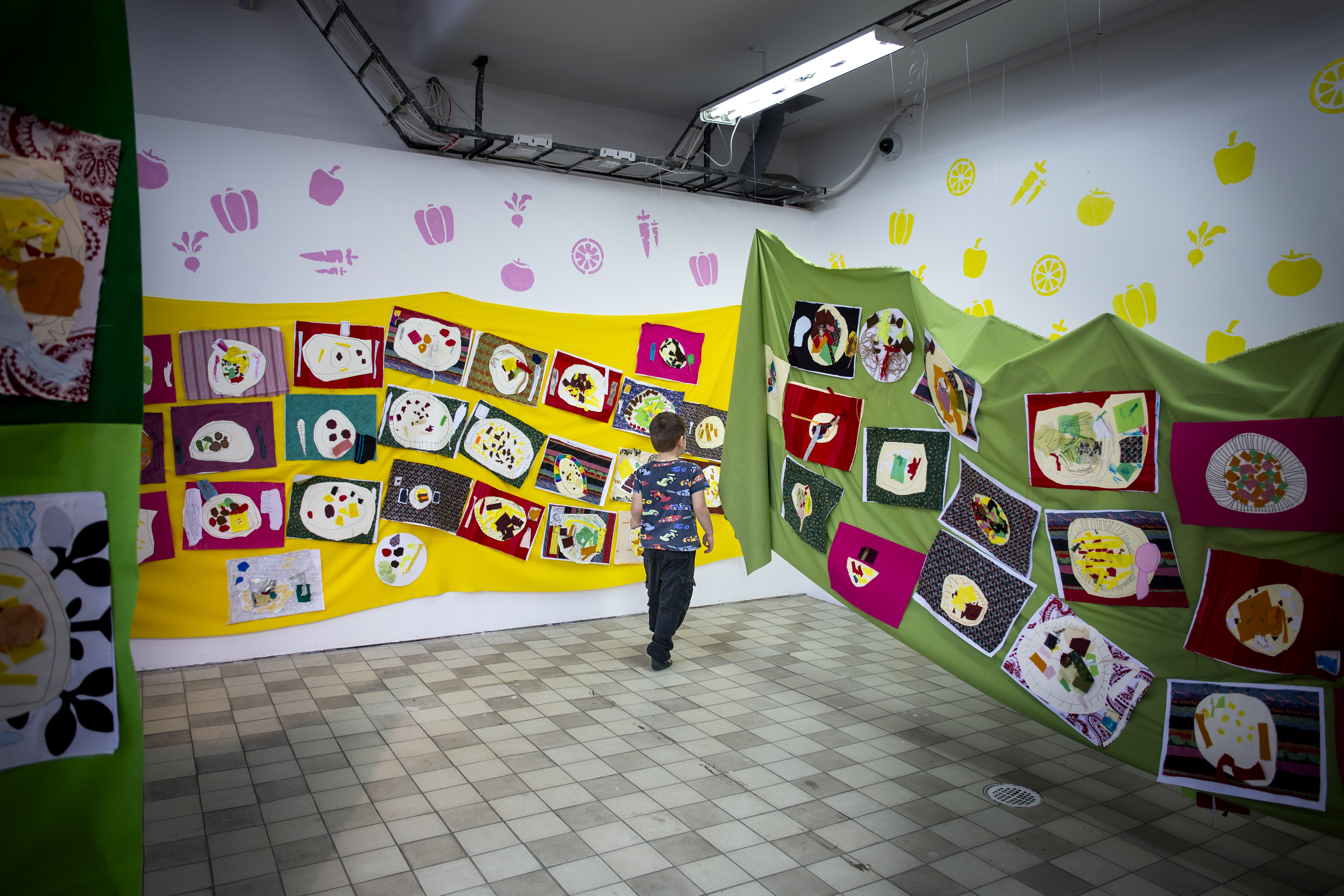 Ett barn går genom en konstutställning med tygverk uppsatta på gula och gröna bakgrunder.