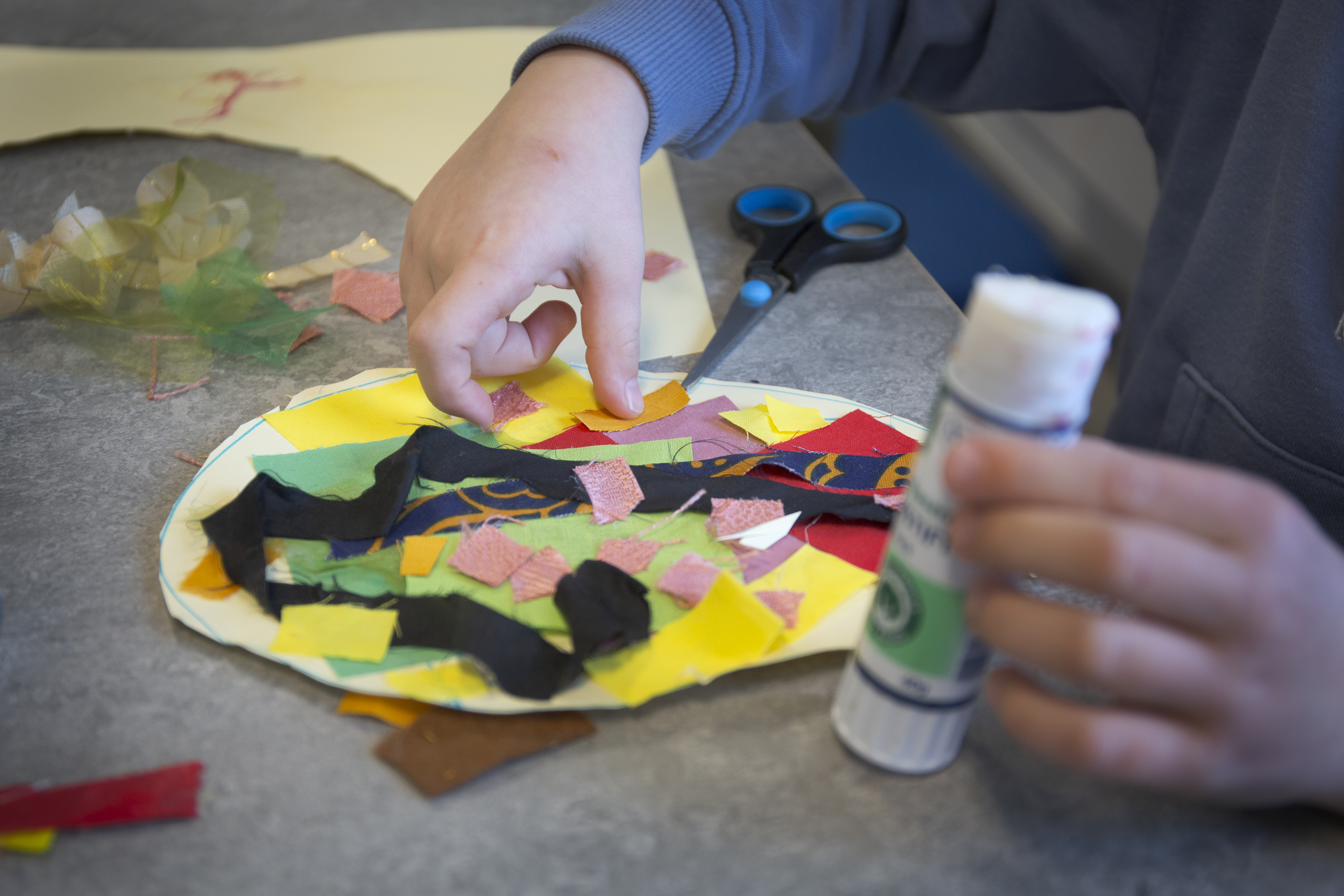 Ett barn använder lim och färgat tyg för att göra ett collage.