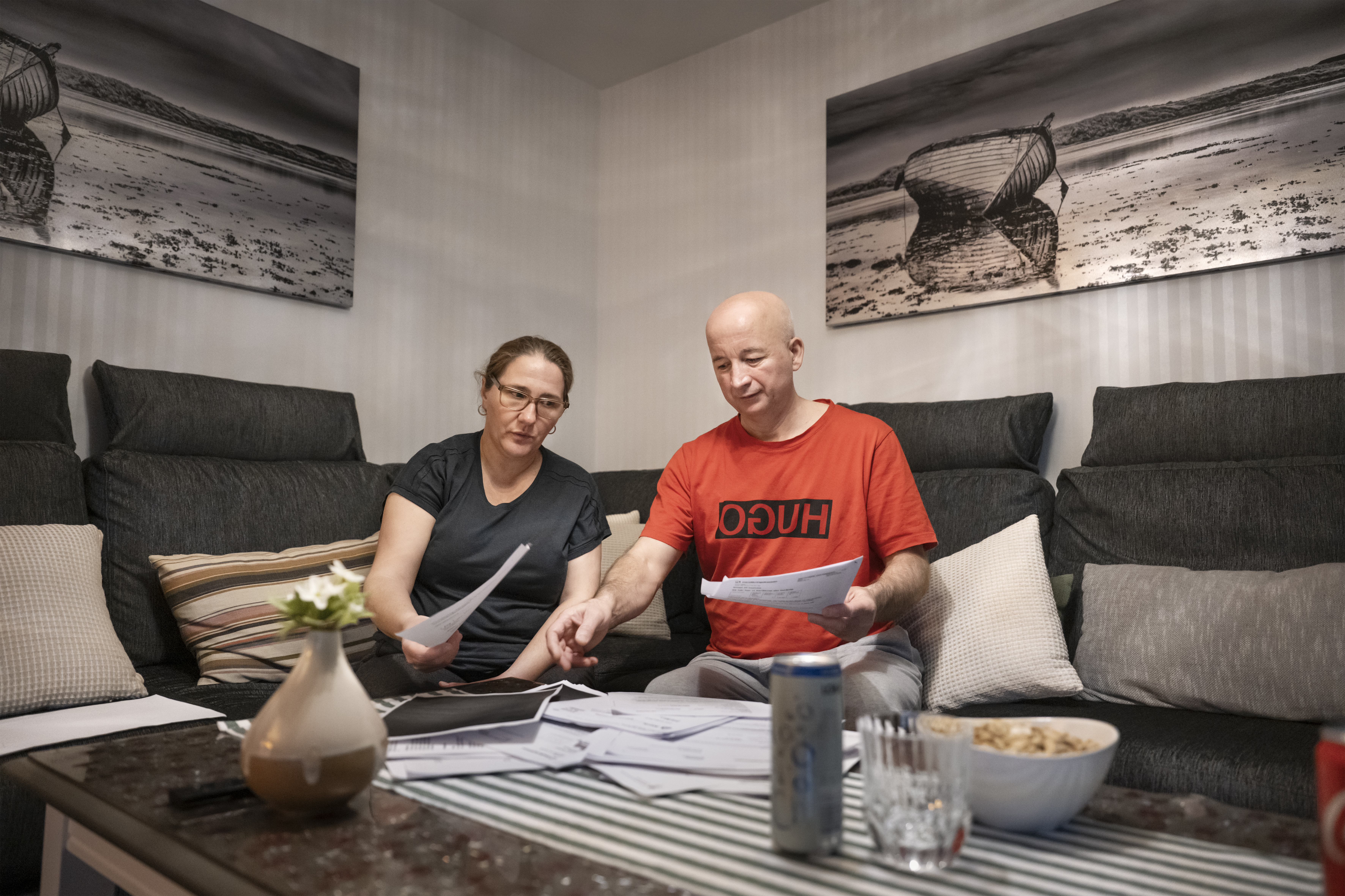 En kvinna och en man sitter i en soffa och går igenom papper som ligger på ett bord framför dem.