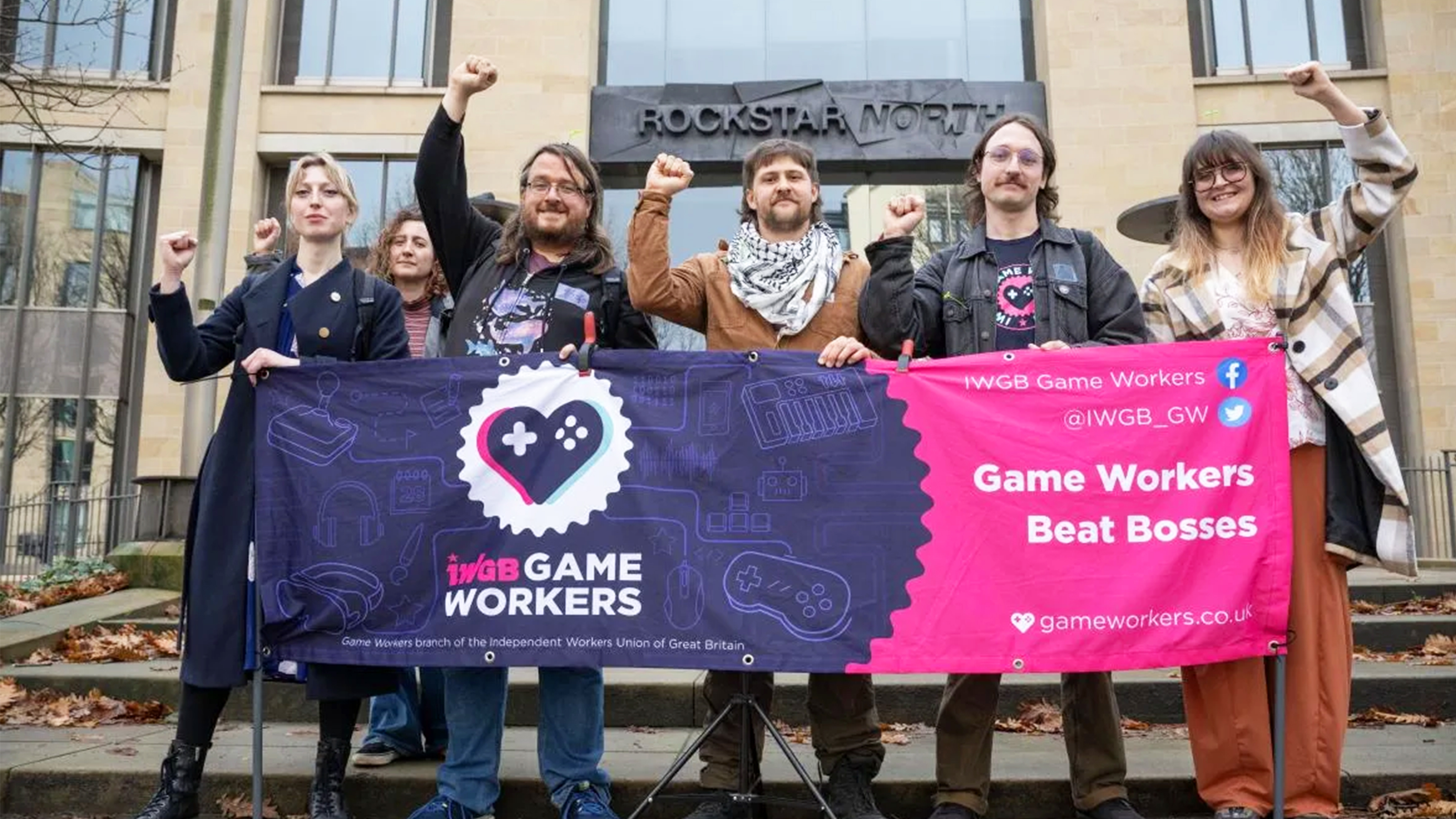 Sex personer höjer nävarna vid en banderoll med fackligt budskap utanför en byggnad.