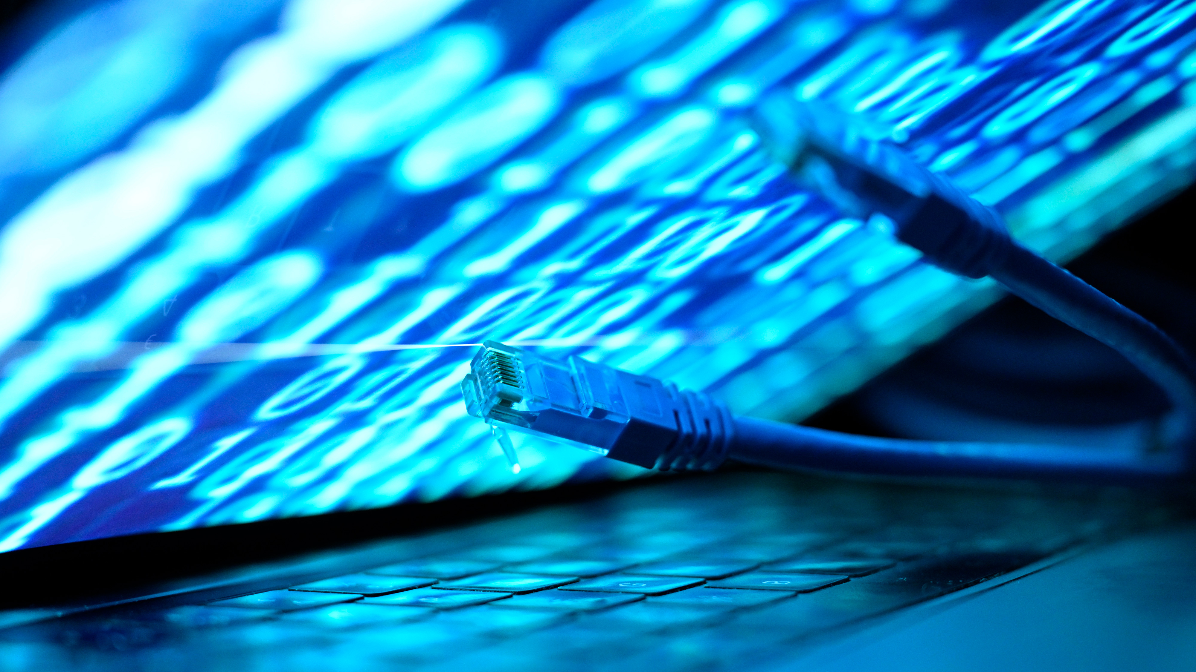 En nätverkskabel ligger på ett laptop-tangentbord, med binär kod synlig i bakgrunden.