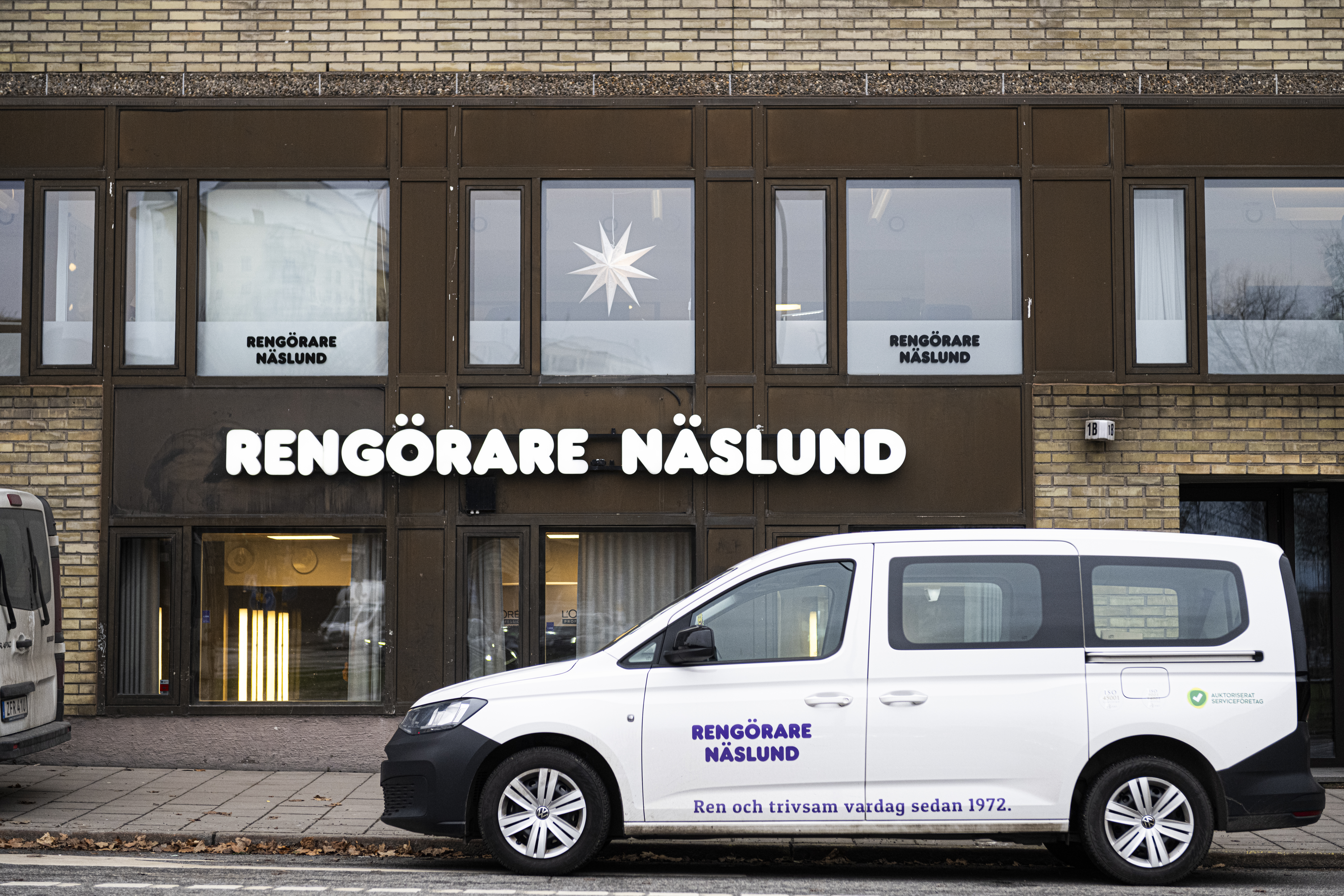 En skåpbil med texten "Rengörare Näslund" är parkerad framför en byggnad där samma namn står på fönstren och fasaden.