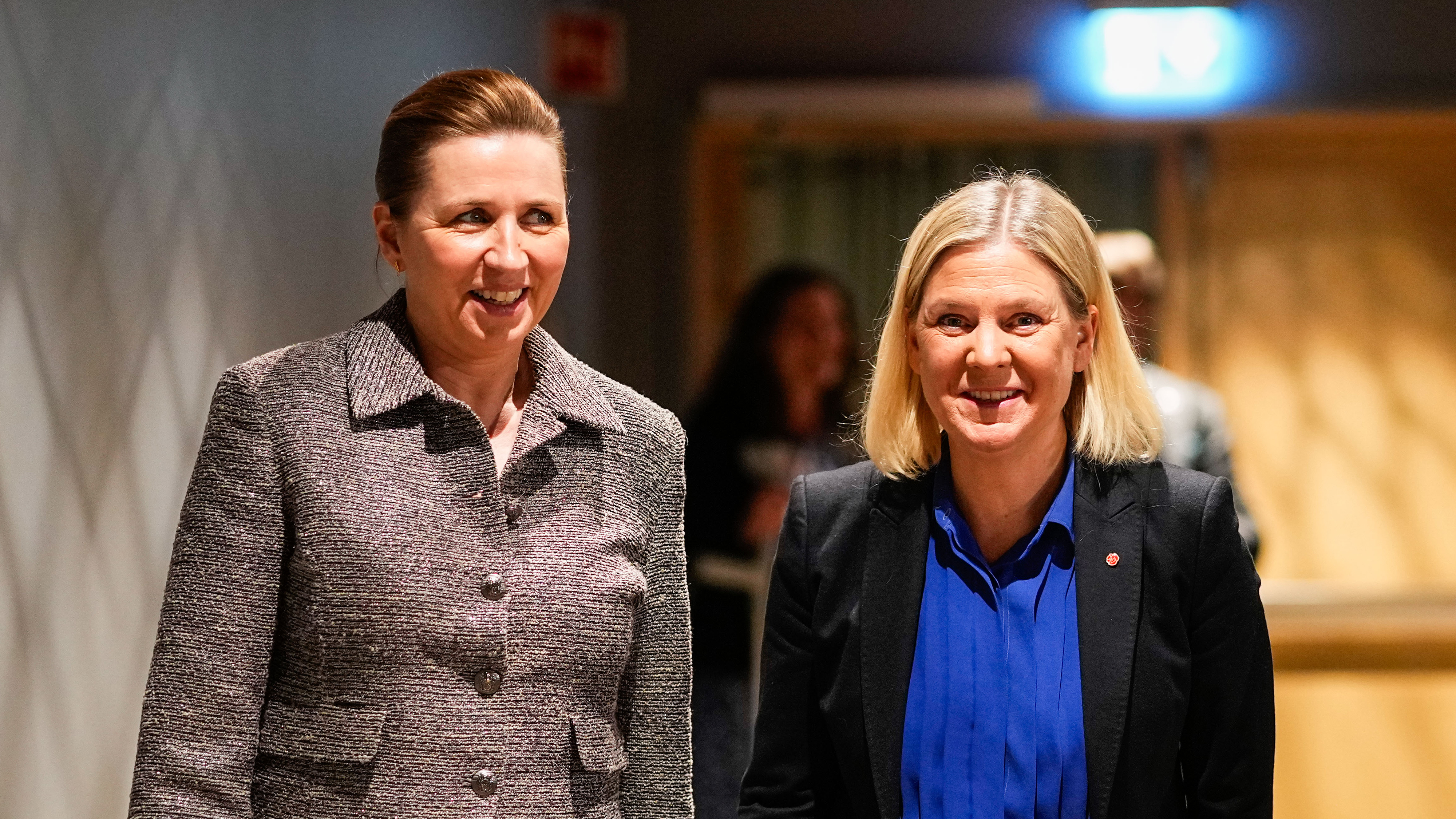 Två kvinnor i affärskläder står inomhus och ser mot kameran; en har grå kavaj, den andra blå blus under svart kavaj.