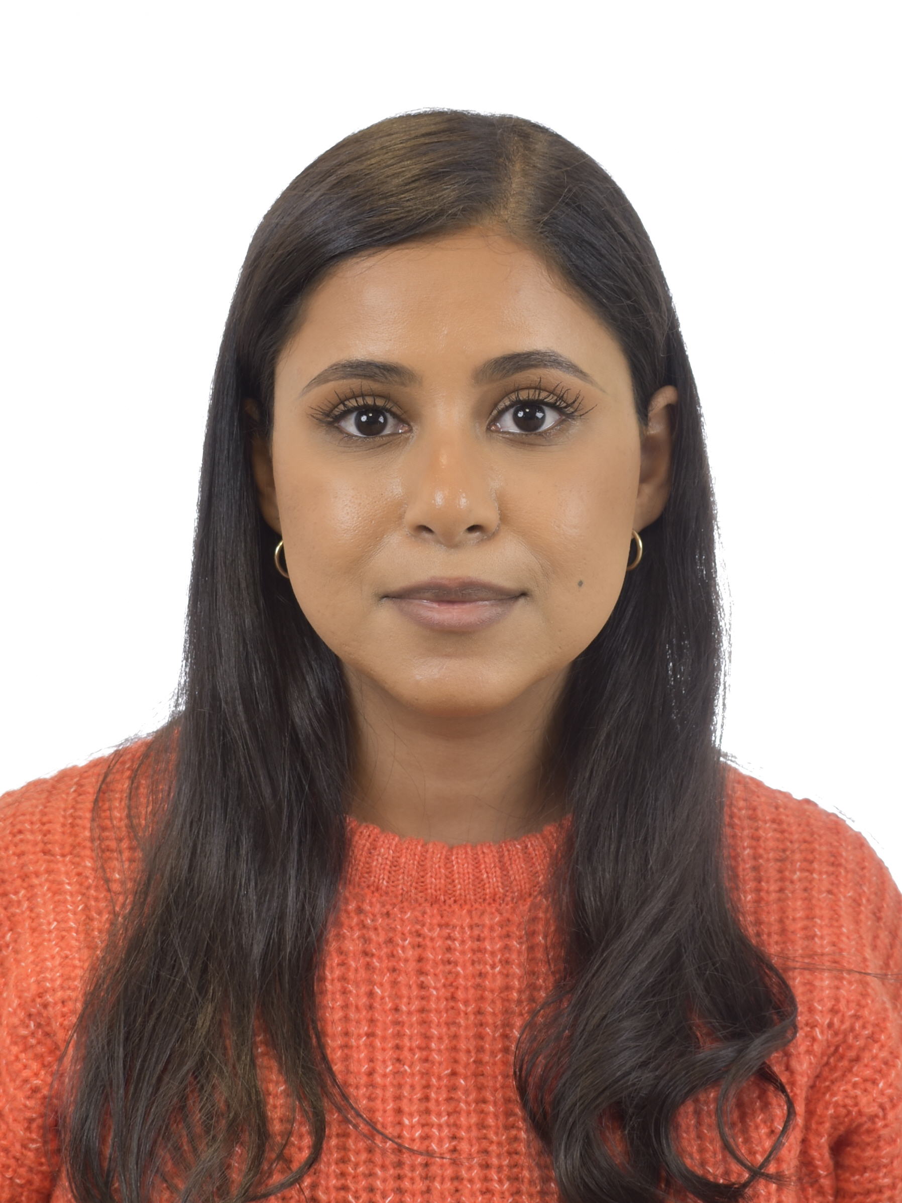 En kvinna med långt mörkt hår har på sig en röd stickad tröja och små ringörhängen, vänd framåt mot en vit bakgrund.