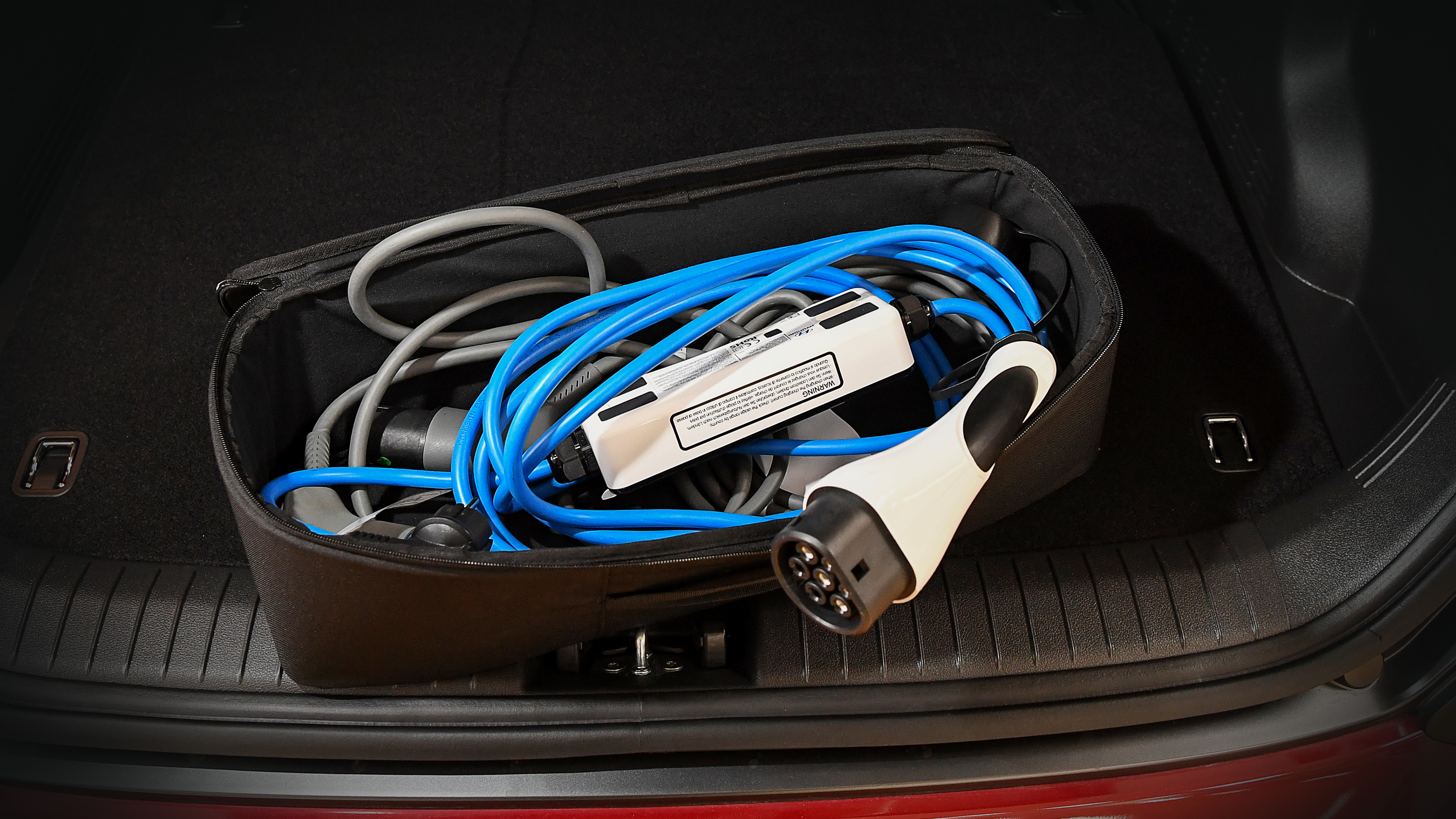 En blå elbilsladdningskabel med kontakt ligger i ett svart fodral i bagageutrymmet på en bil.