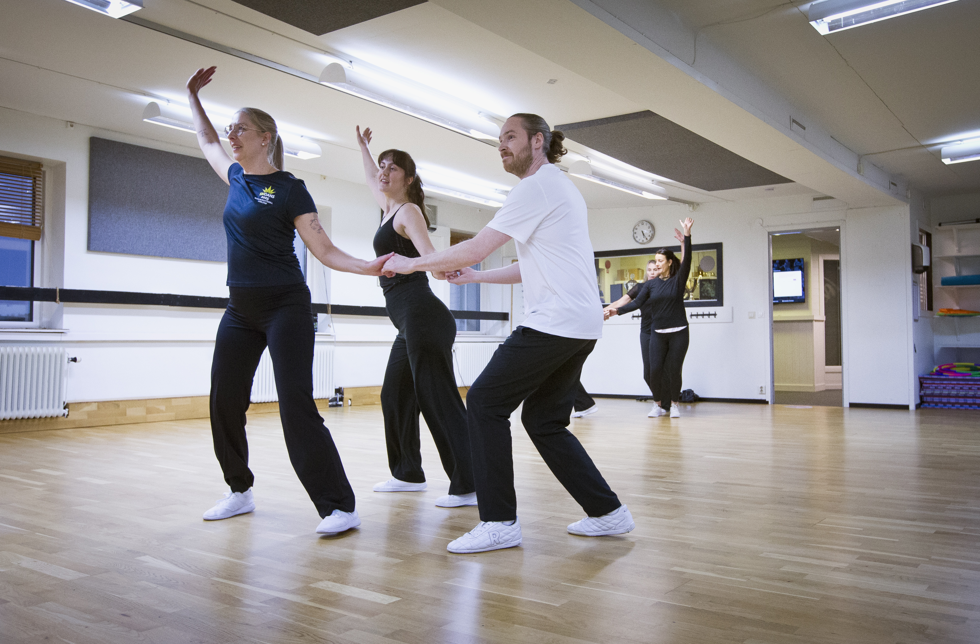 Fyra personer övar en dansrutin i en studio med trägolv och speglar.