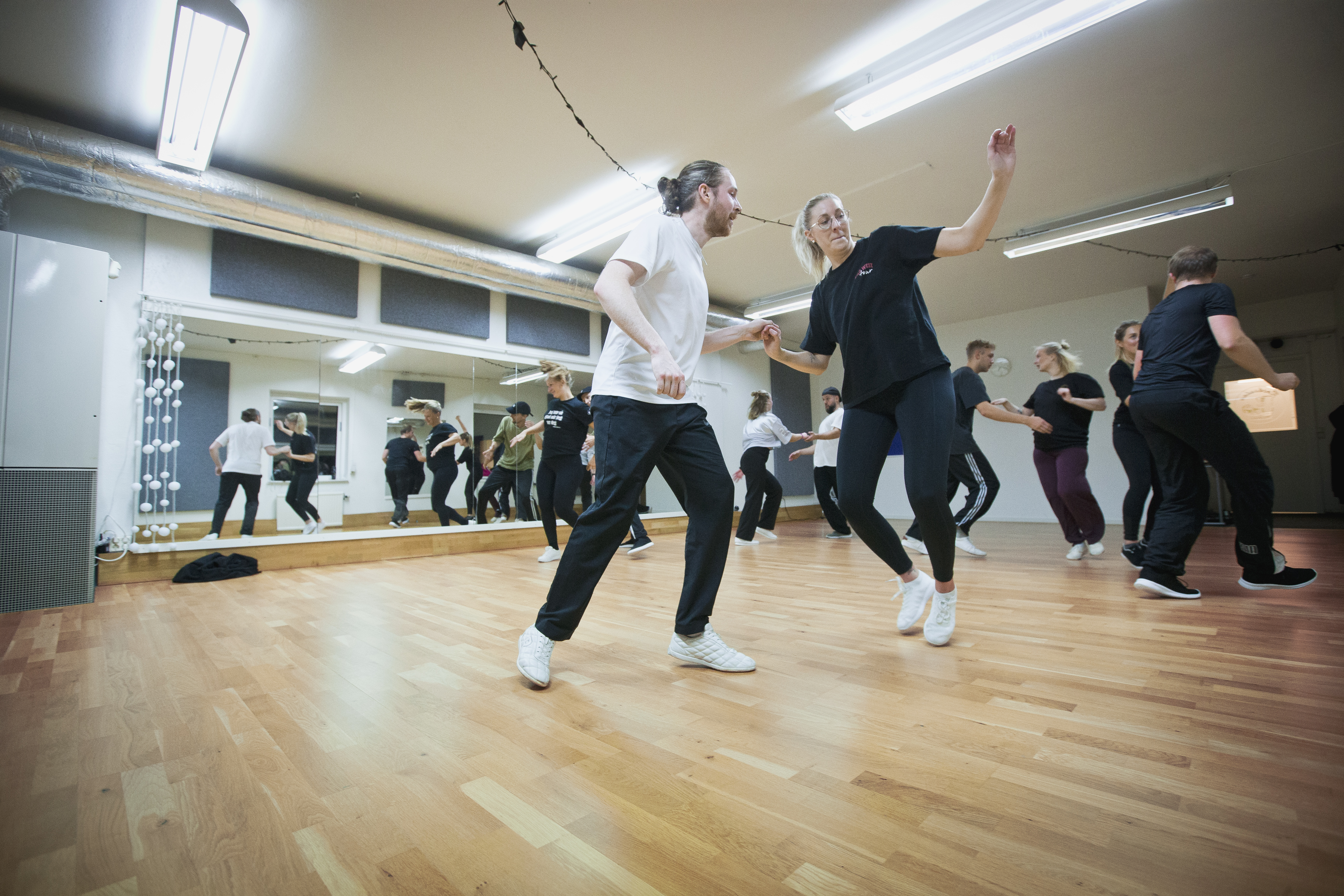 En grupp personer dansar pardans i en studio med trägolv och spegelväggar.