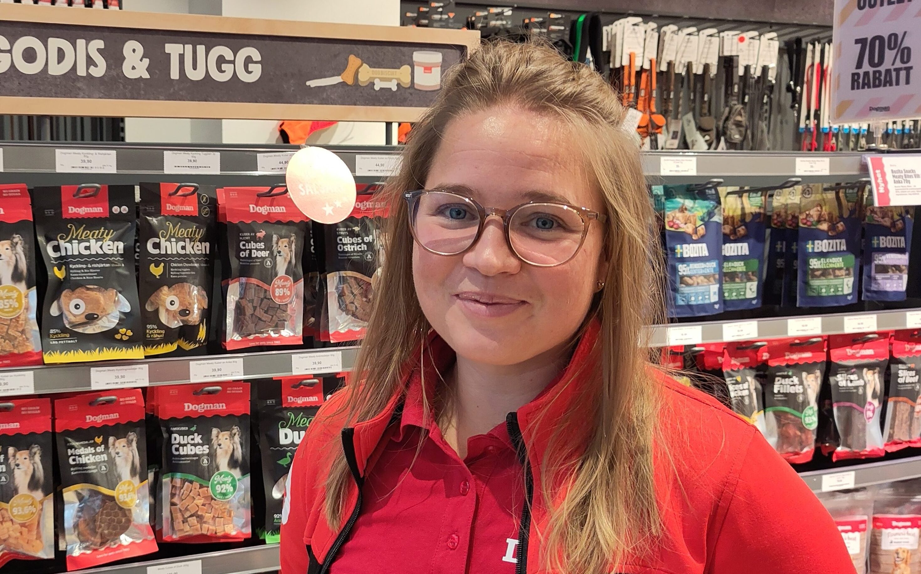 En kvinna med glasögon och röd tröja står framför hyllor med djurgodis i en butik.