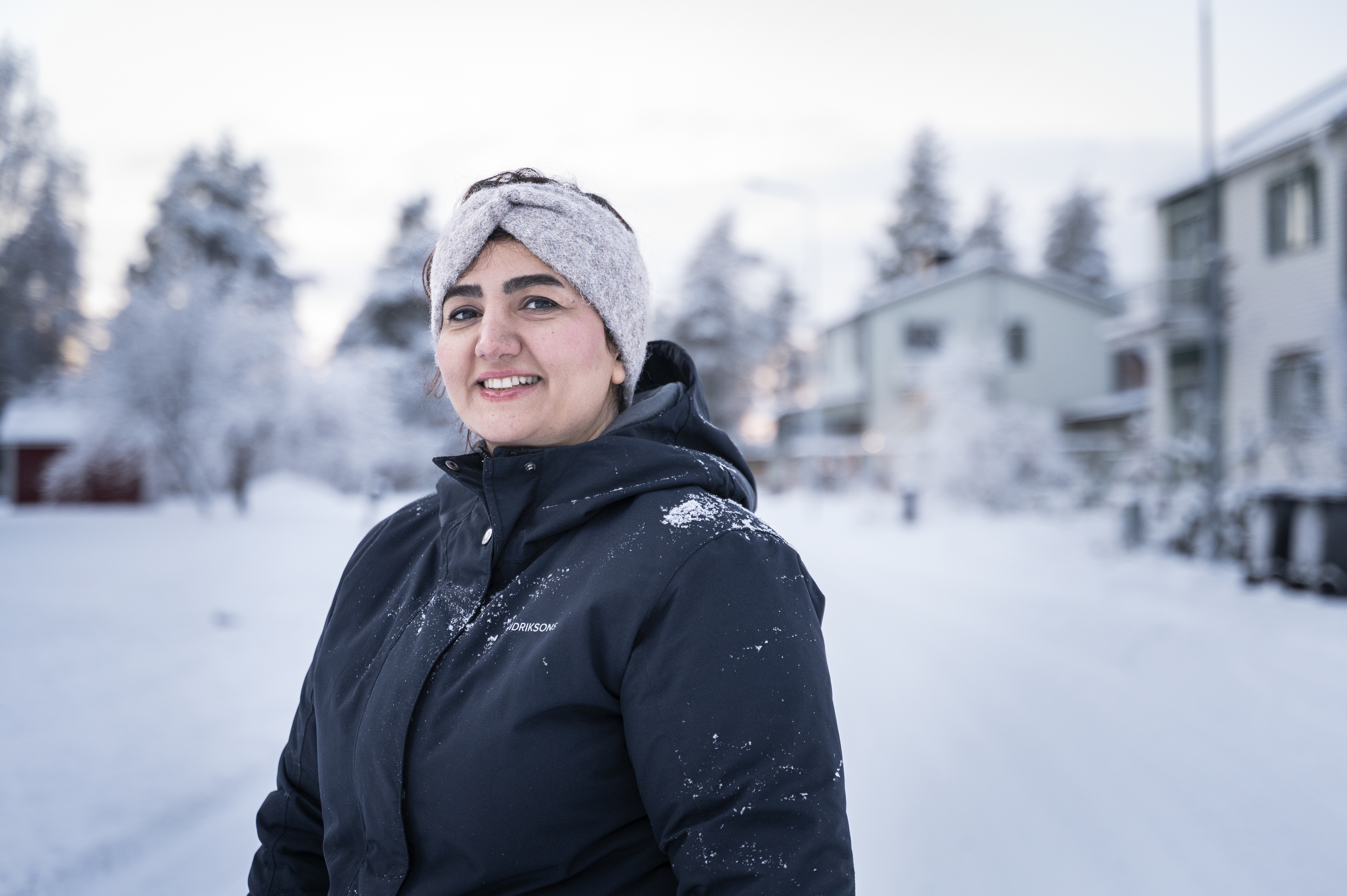 Zahra Vakilbashi med svart vinterjacka och grått pannband står utomhus på en snötäckt gata med hus och träd i bakgrunden.