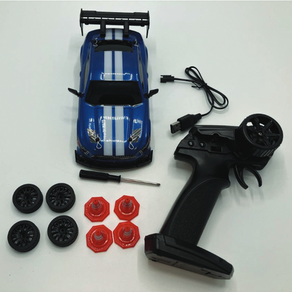 En blå leksaksbil med spoiler, fjärrkontroll, USB-laddsladd, skruvmejsel, fyra extra hjul och fyra orangea hjulkåpor på vit yta.