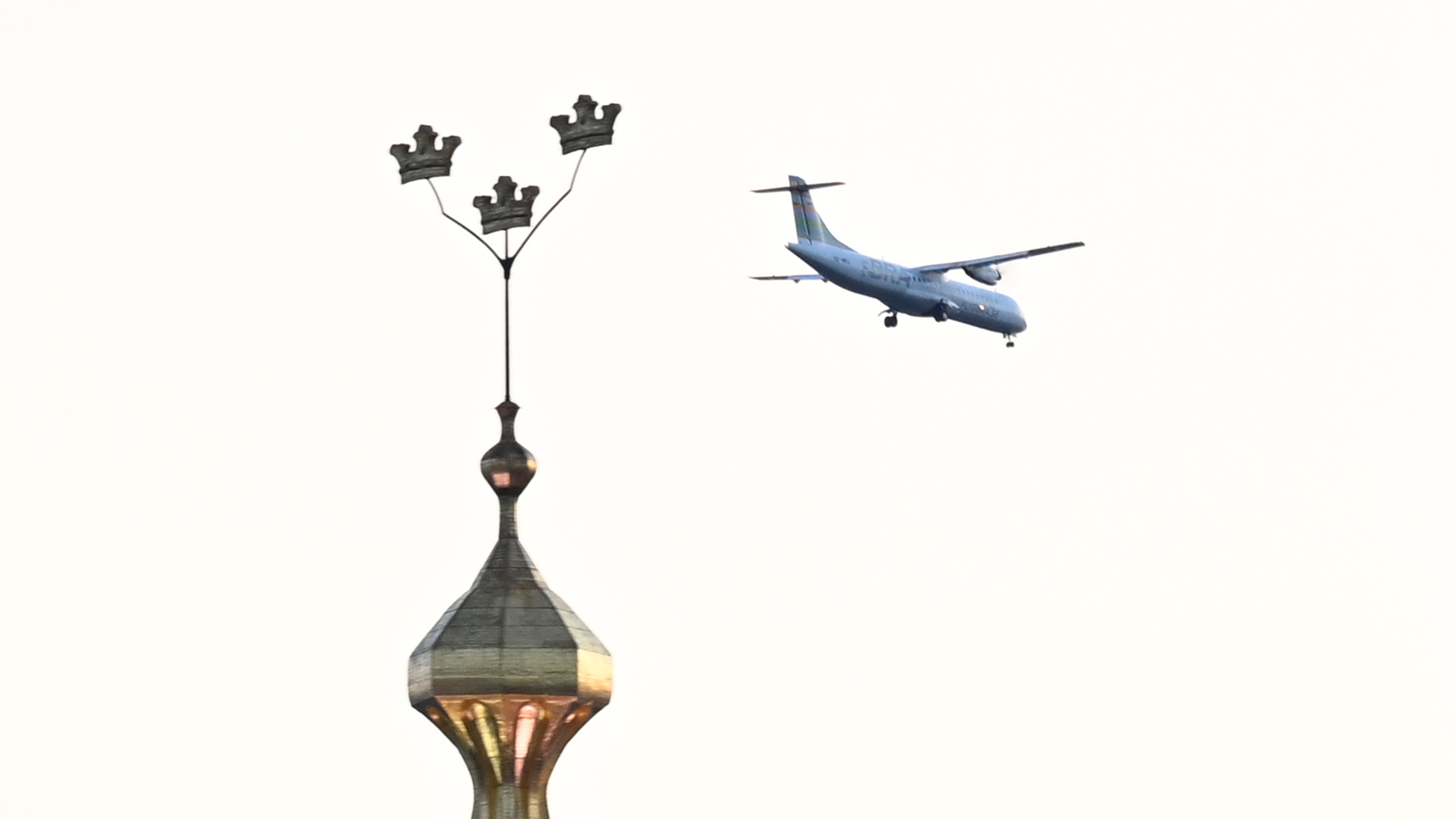 Ett flygplan flyger nära byggnadens tak och håller en spira och tre kronor.
