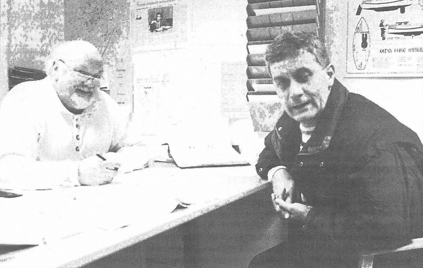 Två män sitter vid ett skrivbord på ett kontor; en skriver medan den andre tittar mot kameran.