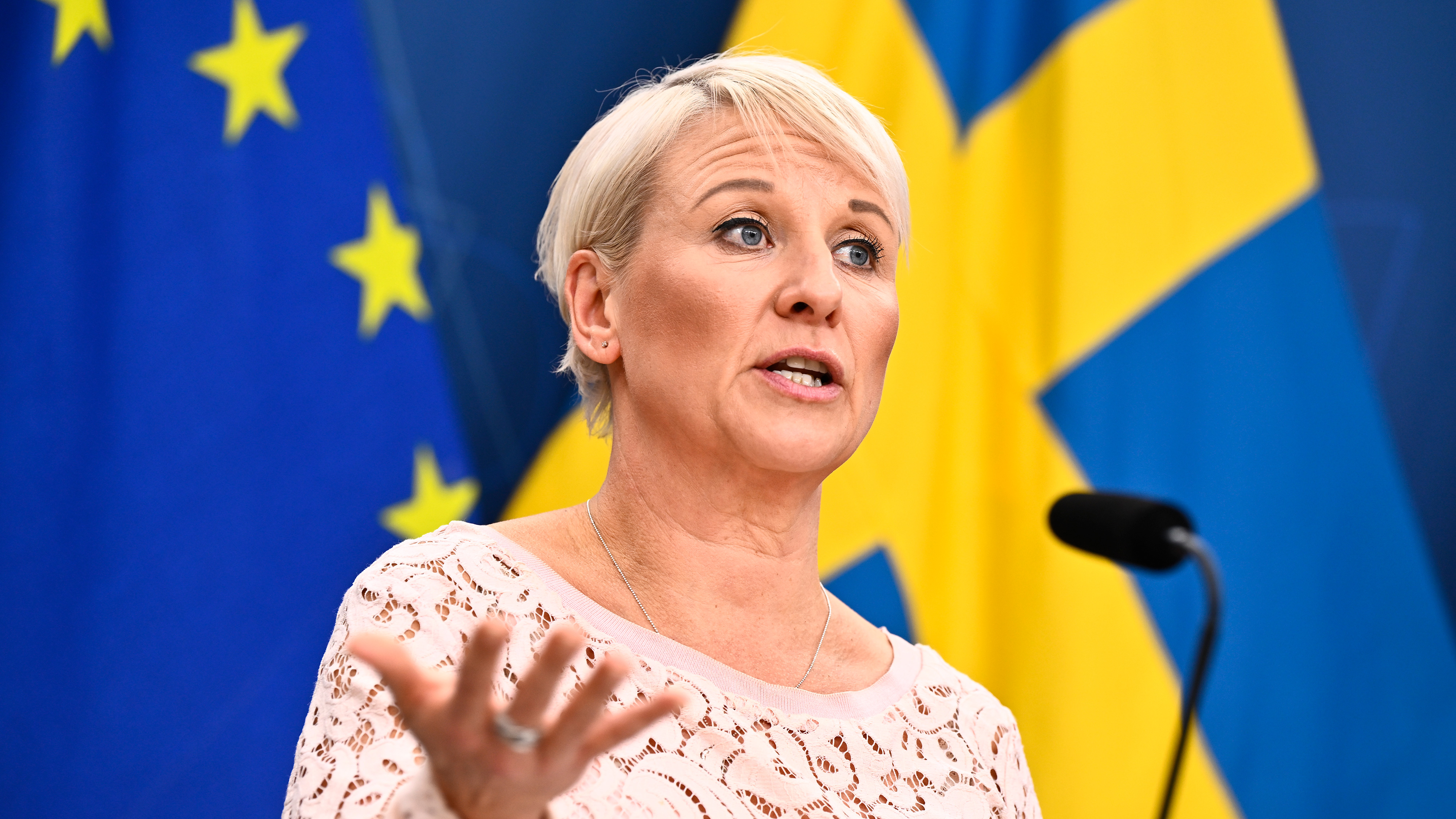Äldre- och socialförsäkringsminister Anna Tenje (M) med Sverige och EU:s flagga bakom sig.