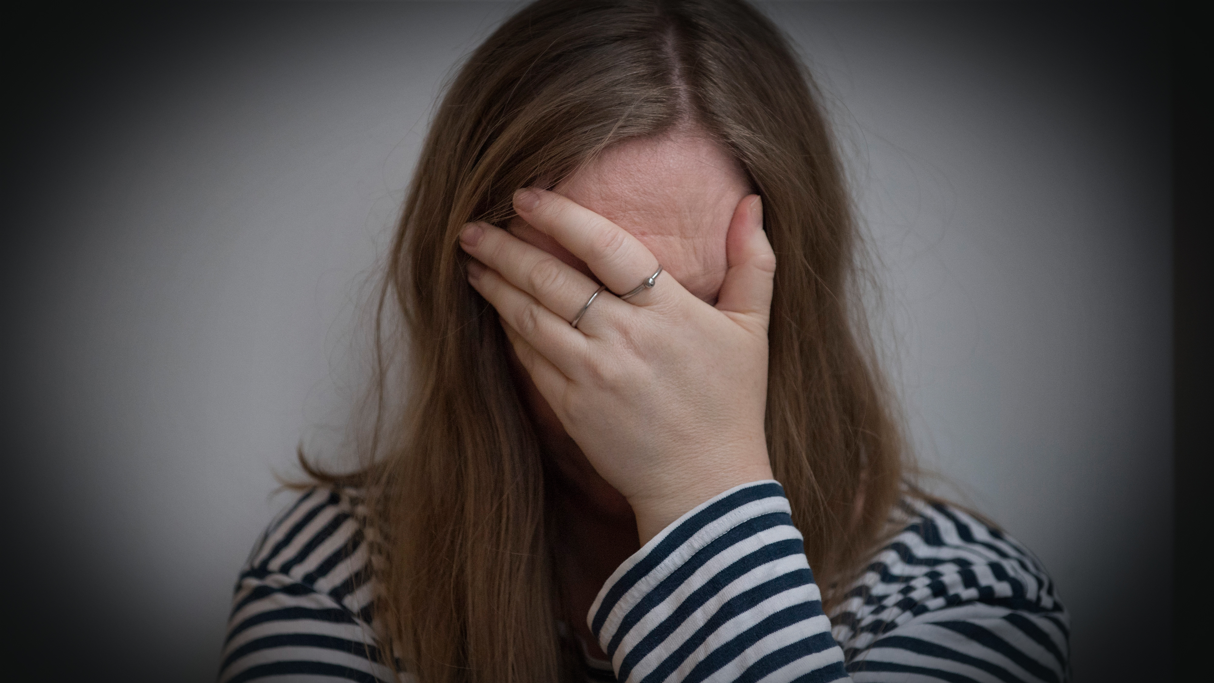 En person med långt hår och randig tröja täcker ansiktet med ena handen så att ansiktsuttrycket inte syns.