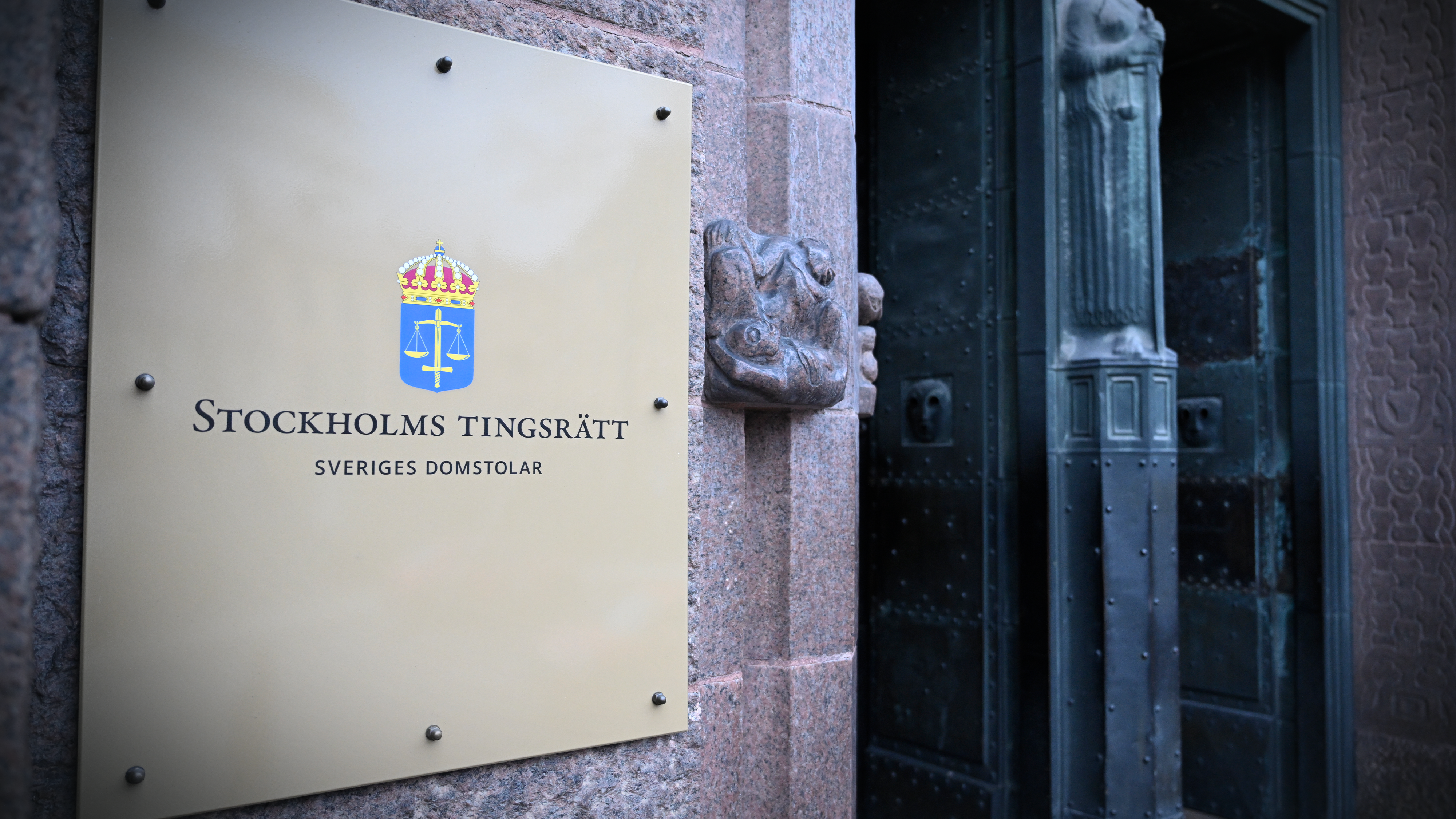 En skylt med texten "Stockholms tingsrätt Sveriges Domstolar" står vid ingången till en byggnad med öppen dörr.