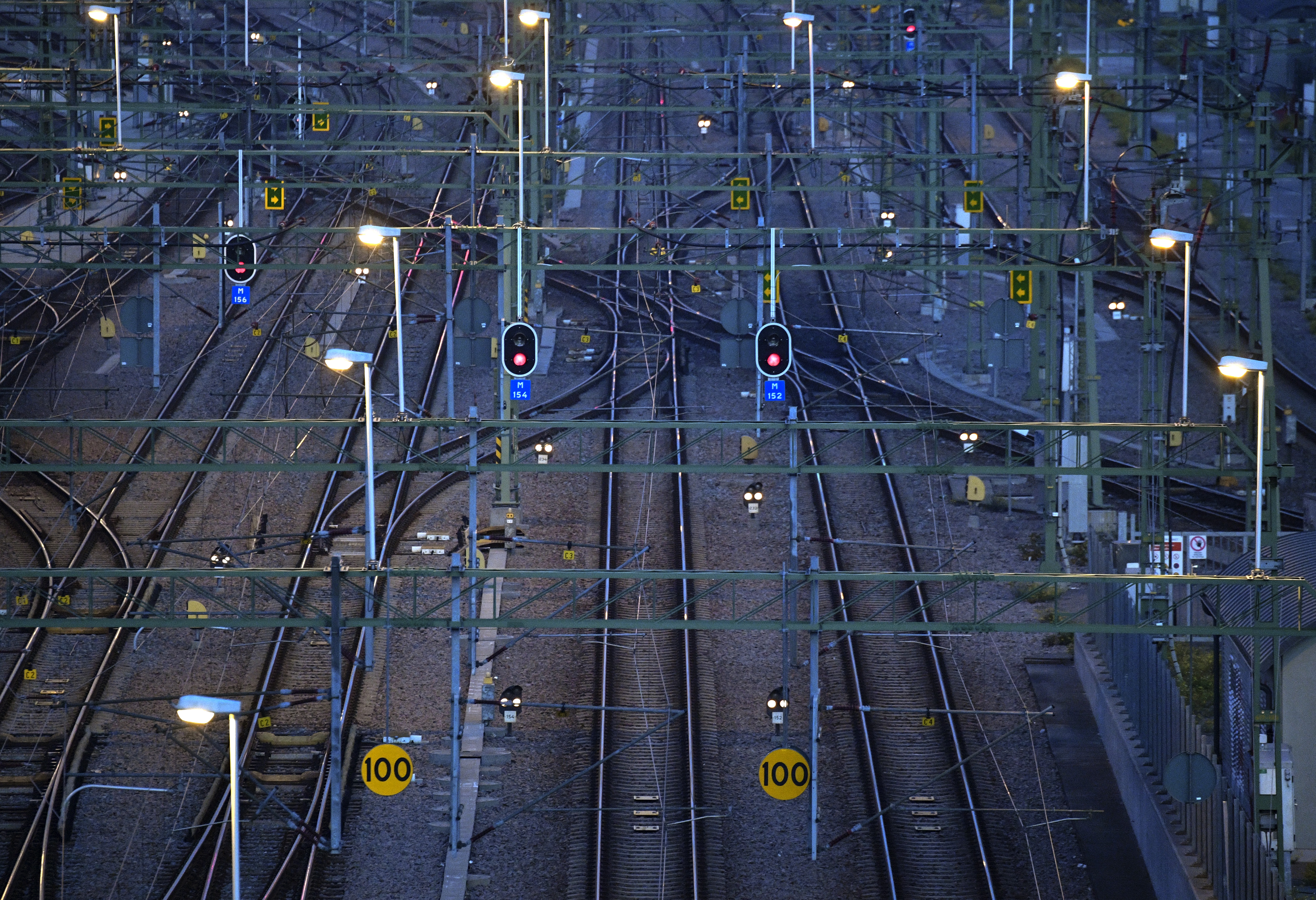 Järnvägsstötfångare med några järnvägsspår, signaler, kraftledningar och ljusstolpar. Vissa trafikljus blir röda. Hastighetsskylten visar 100.