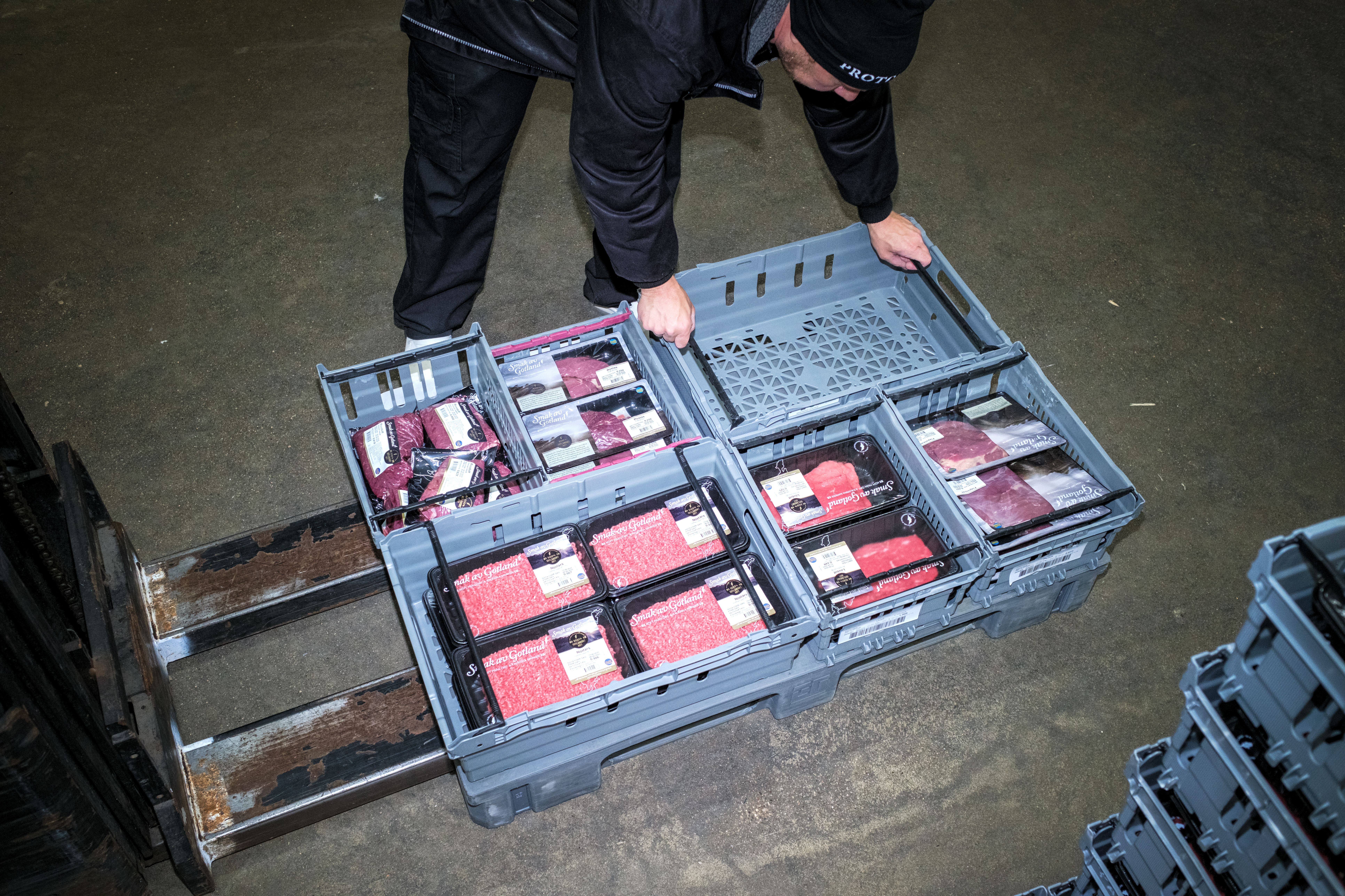 En person lastar plastlådor med förpackat kött på en truck i ett lager.