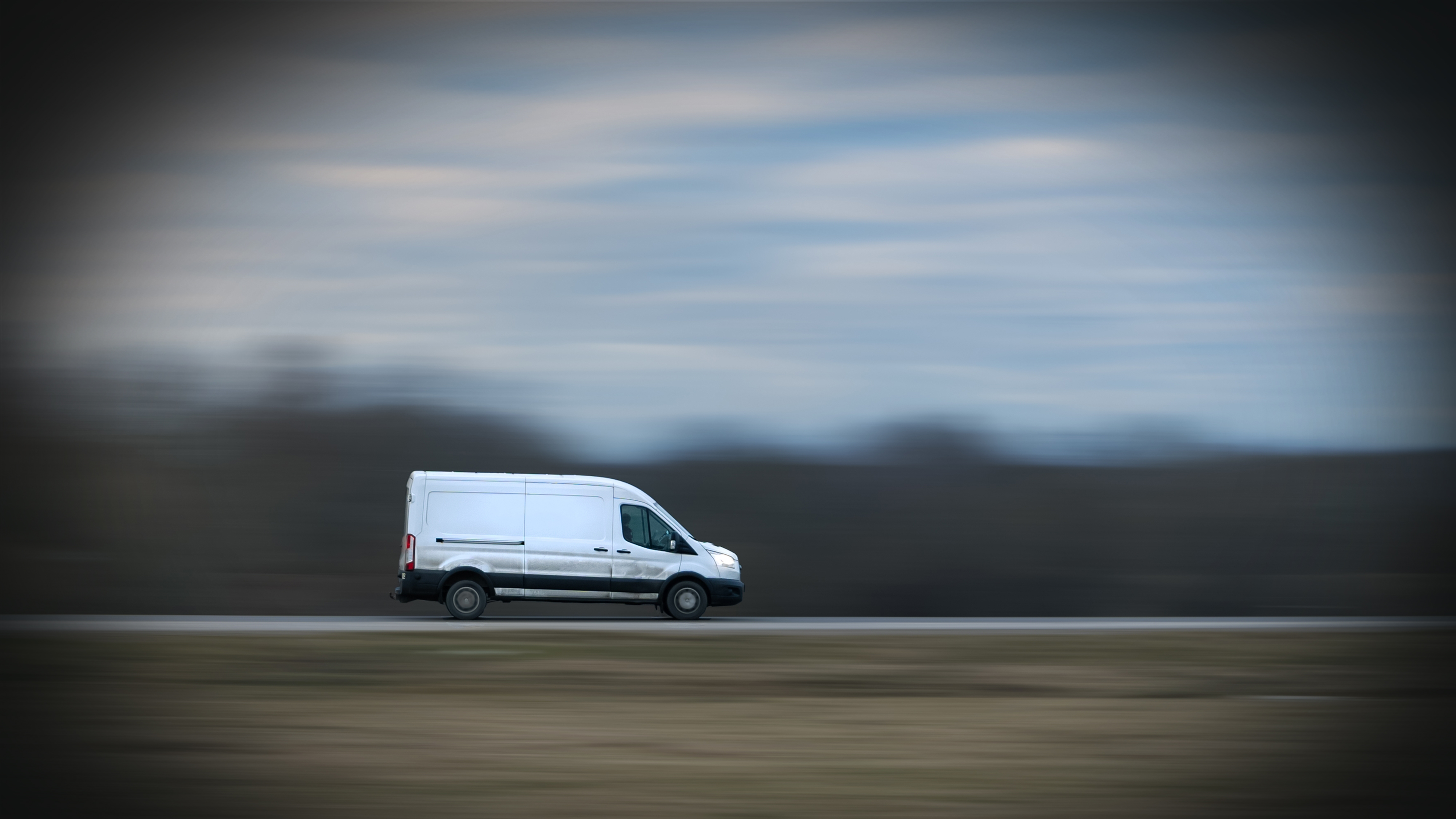 En vit skåpbil kör på en väg med en bakgrund som inte är i fokus.