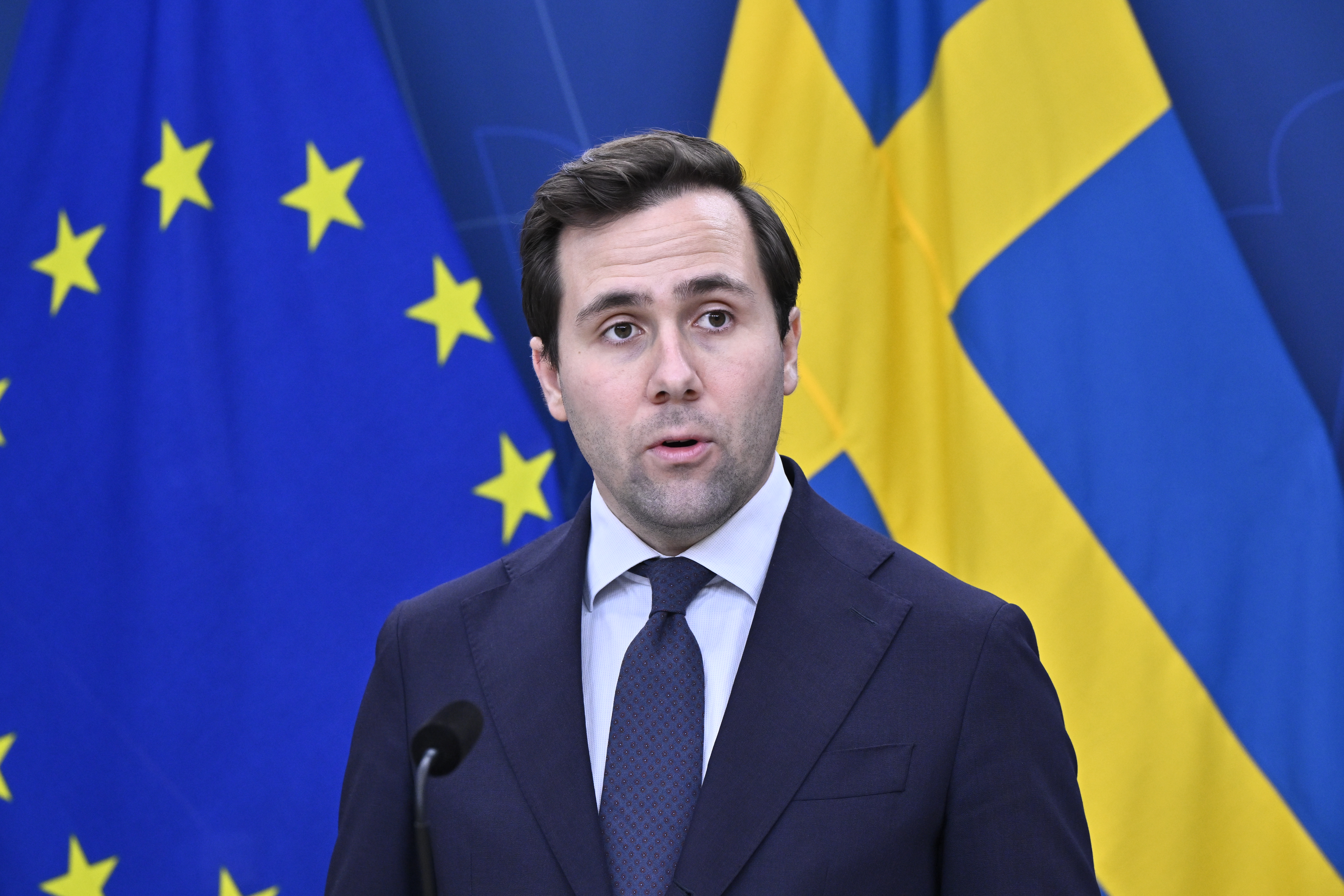 En man i kostym talar vid ett podium framför Europeiska unionens och Sveriges flaggor.