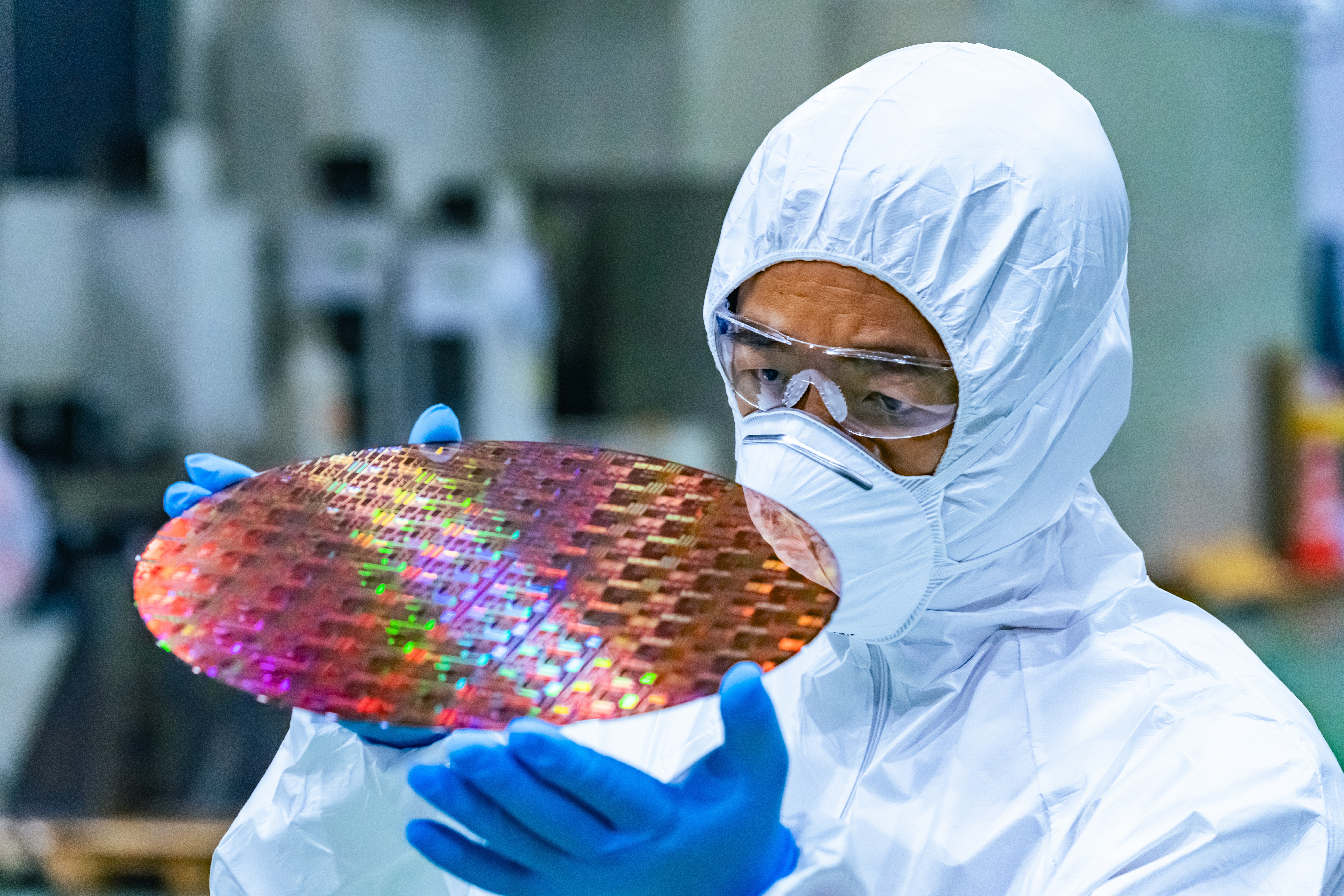En tekniker i skyddsdräkt och handskar undersöker ett kiselchip som används vid tillverkning av halvledare.