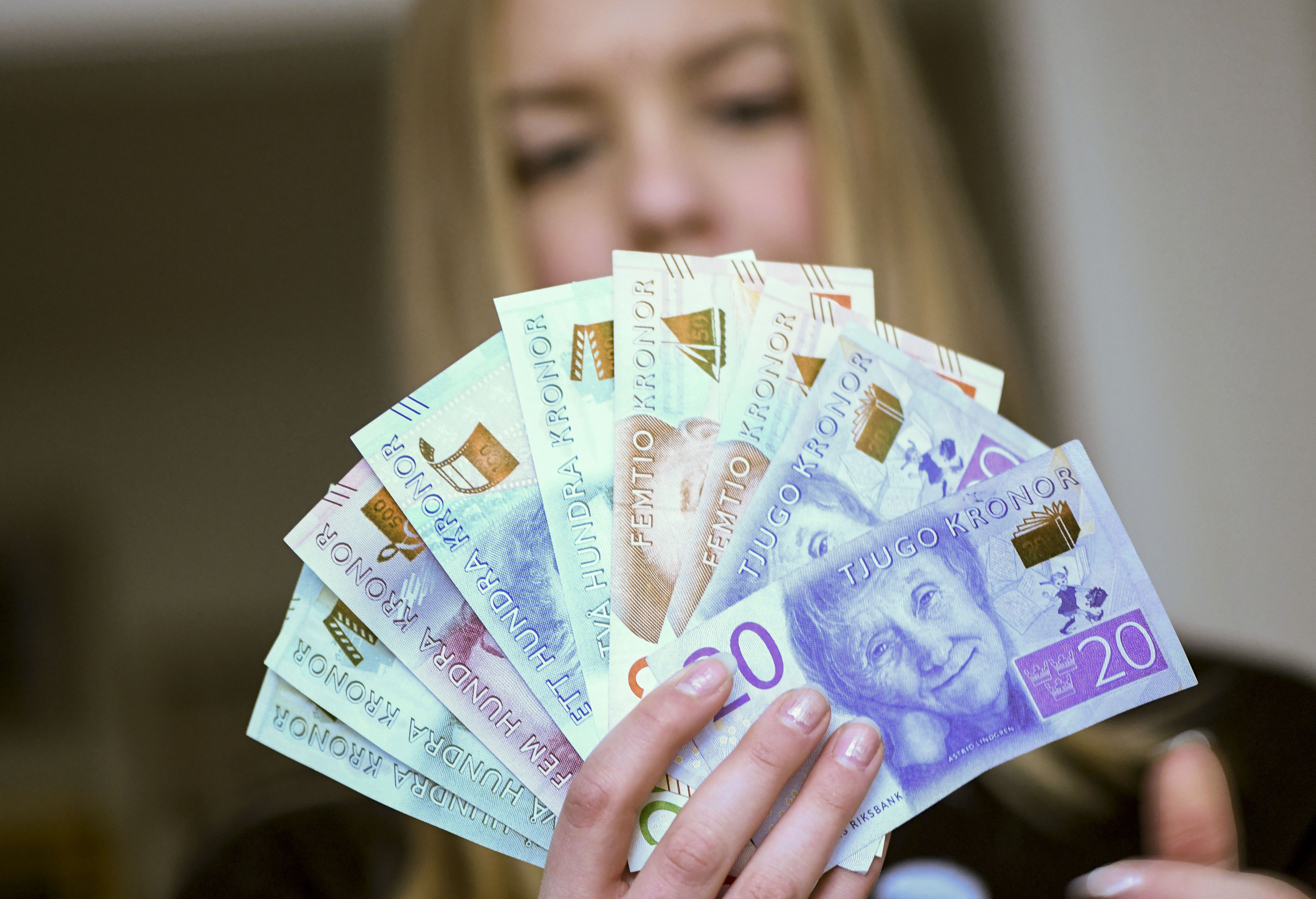 En person som håller ett utspritt knippe svenska kronsedlar av olika valörer.