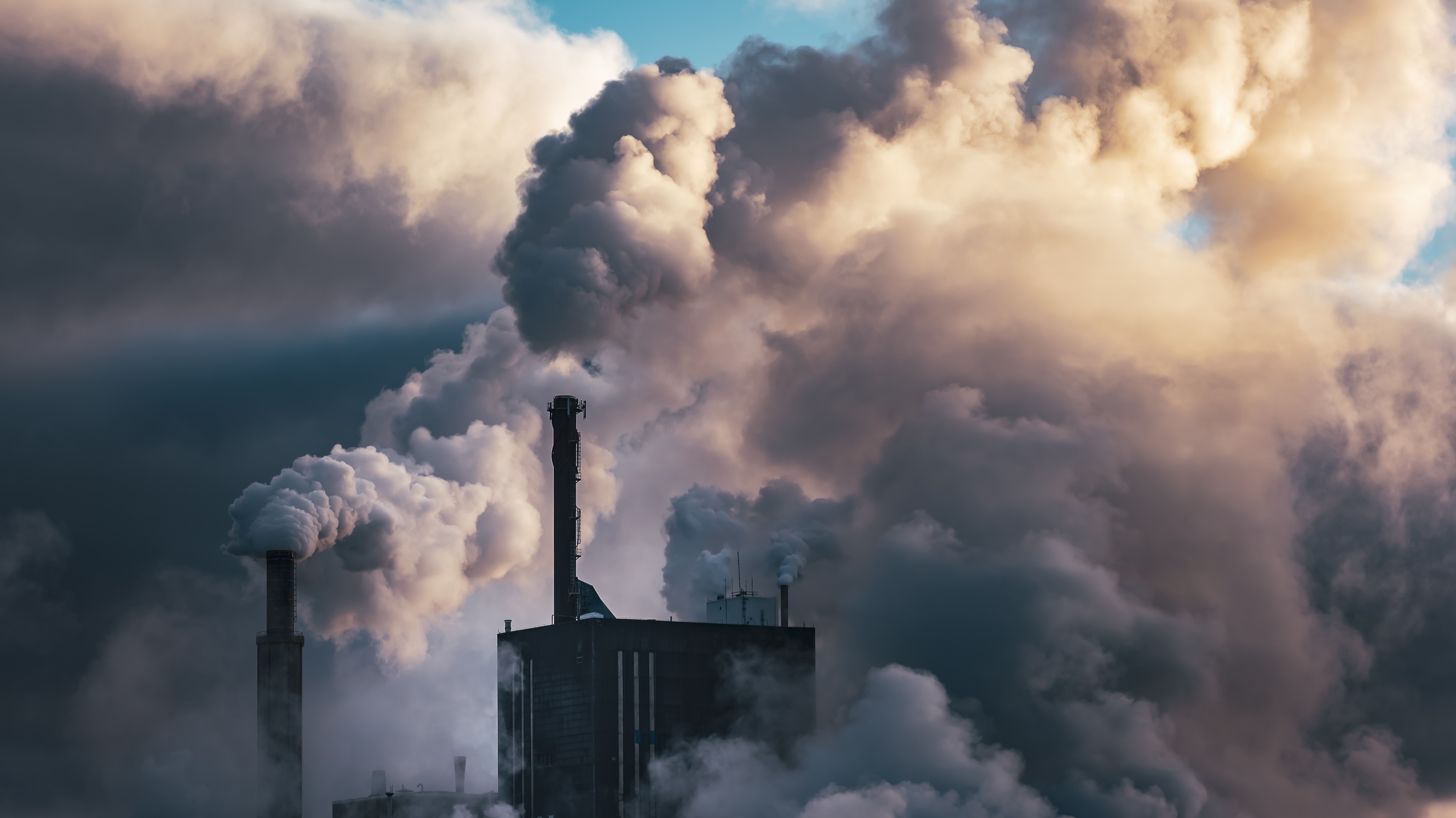 En industriell anläggning släpper ut rök och ånga som täcker delar av byggnaden och samlas i luften runt omkring.