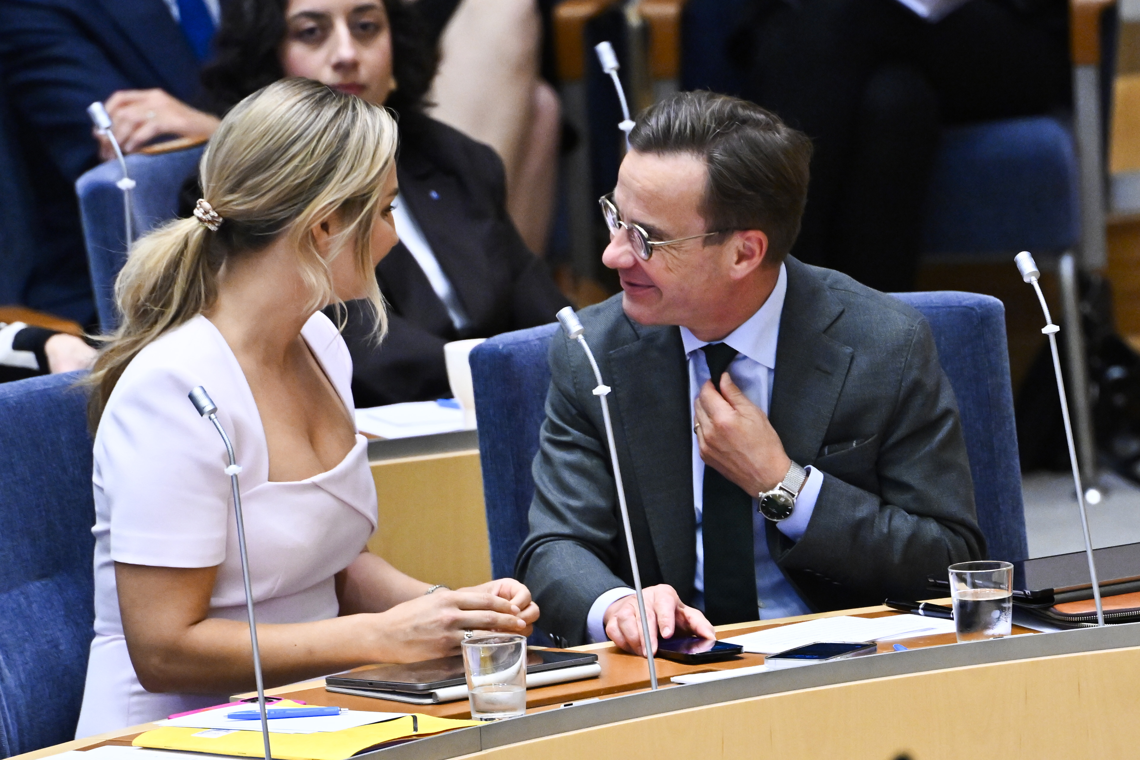 En kvinna och en man i affärskläder sitter vid ett konferensbord och pratar. Det finns papper och vattenglas framför dem.