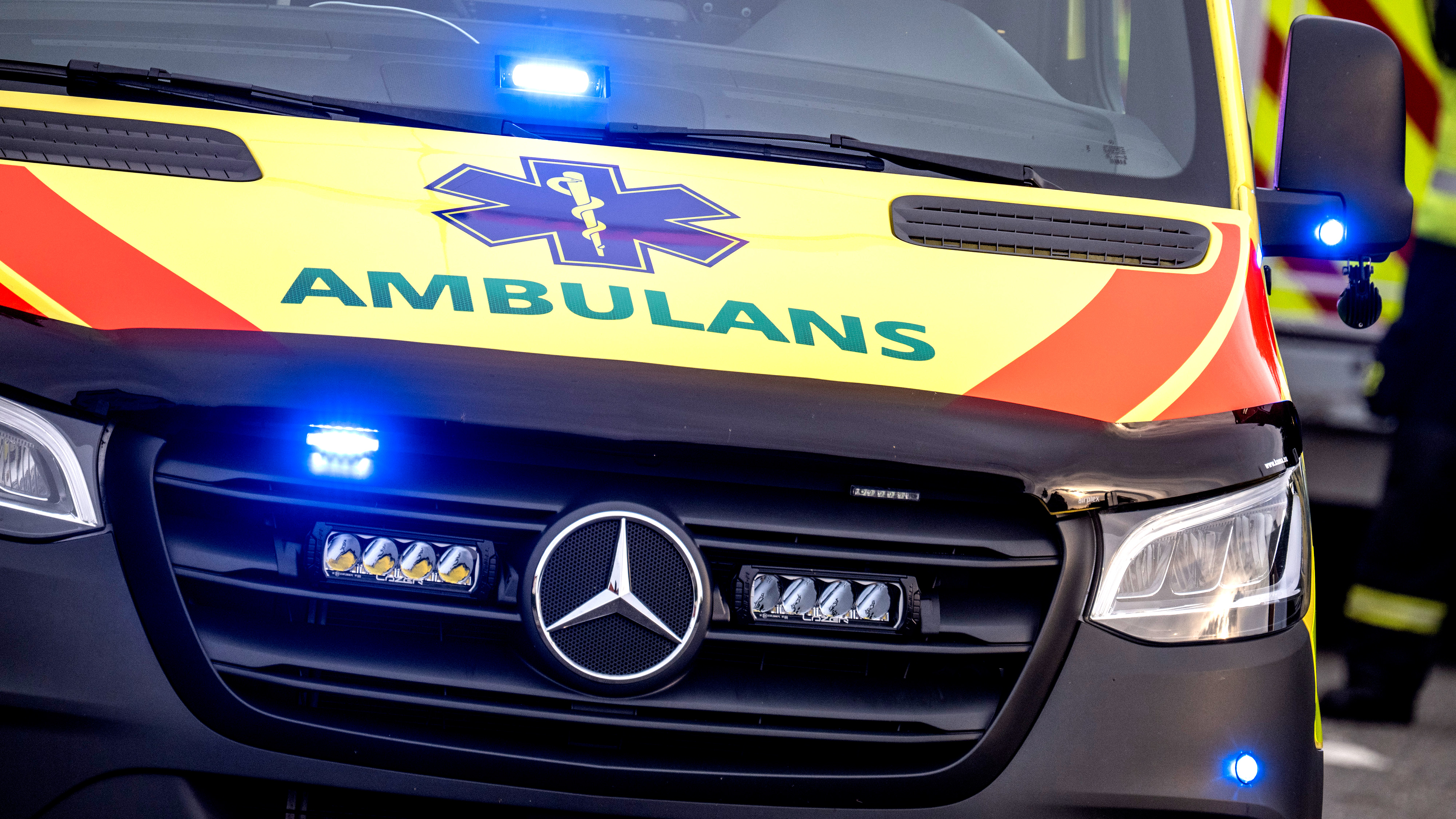 En ambulans i gult med blåljus och texten "Ambulans" på fronten syns.