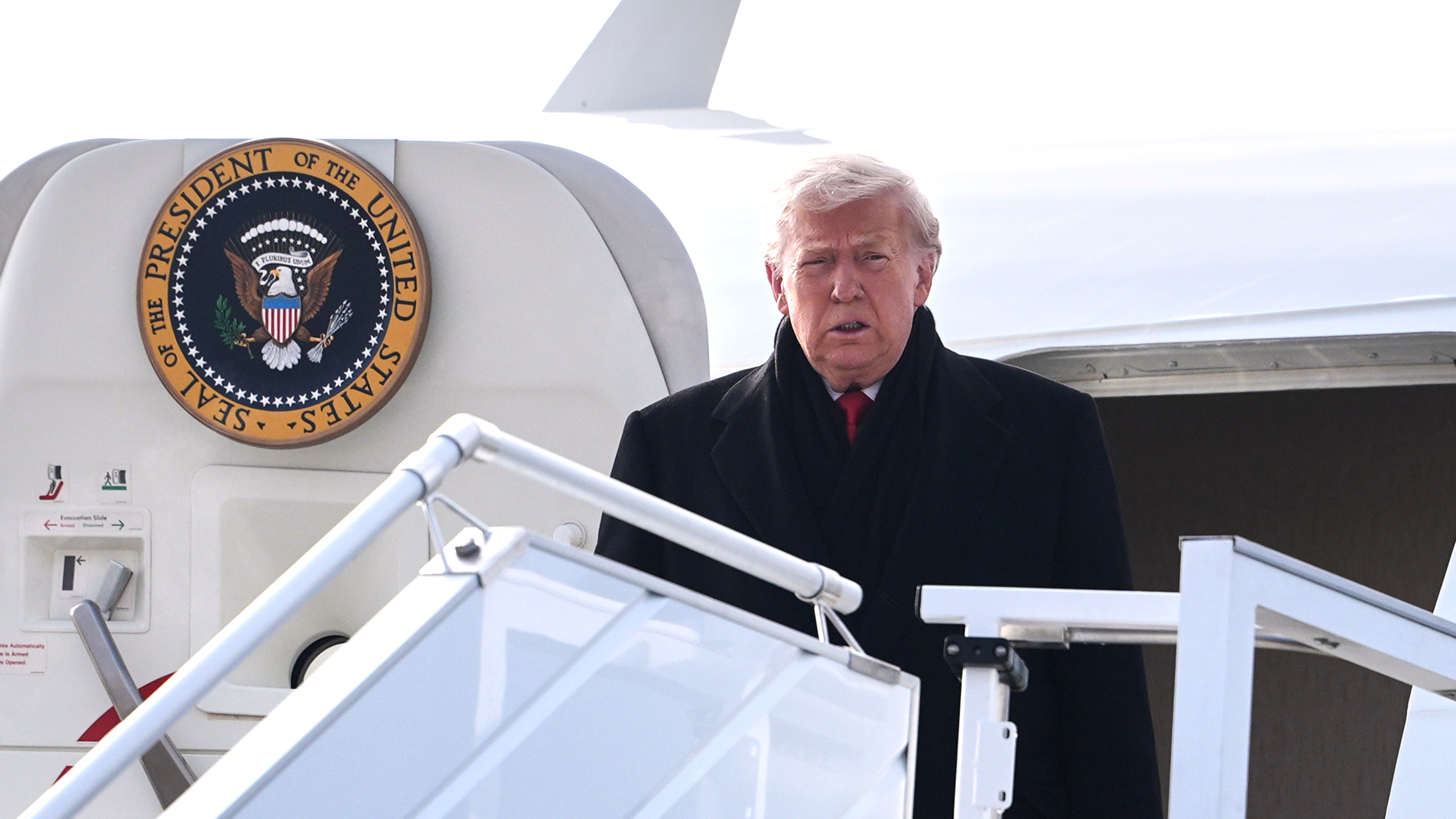 En man i svart rock står högst upp på flygplanstrappan nära en skylt med texten "Seal of the President of the United States".