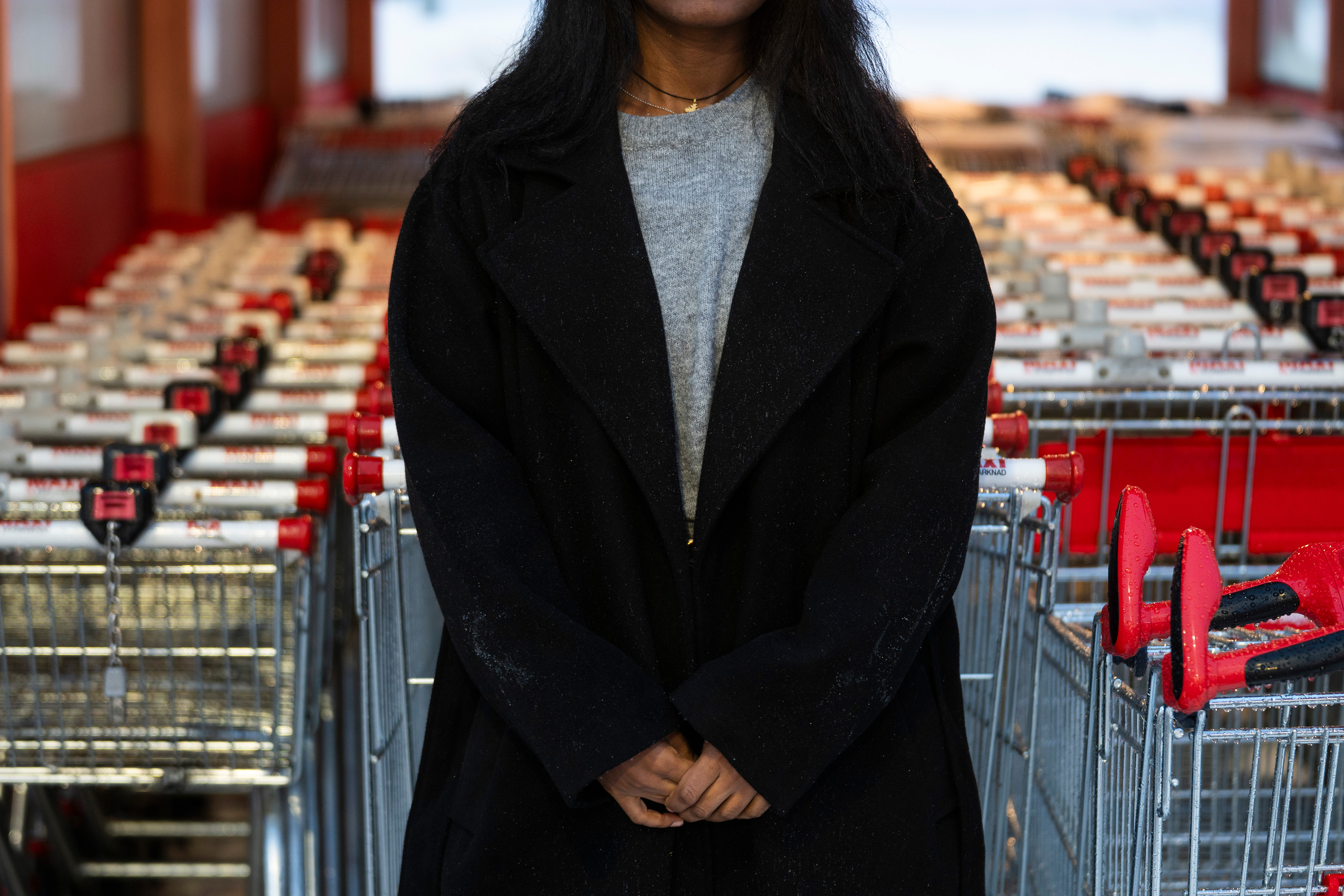 En person med svart rock står framför en rad kundvagnar vid en butiksentré.