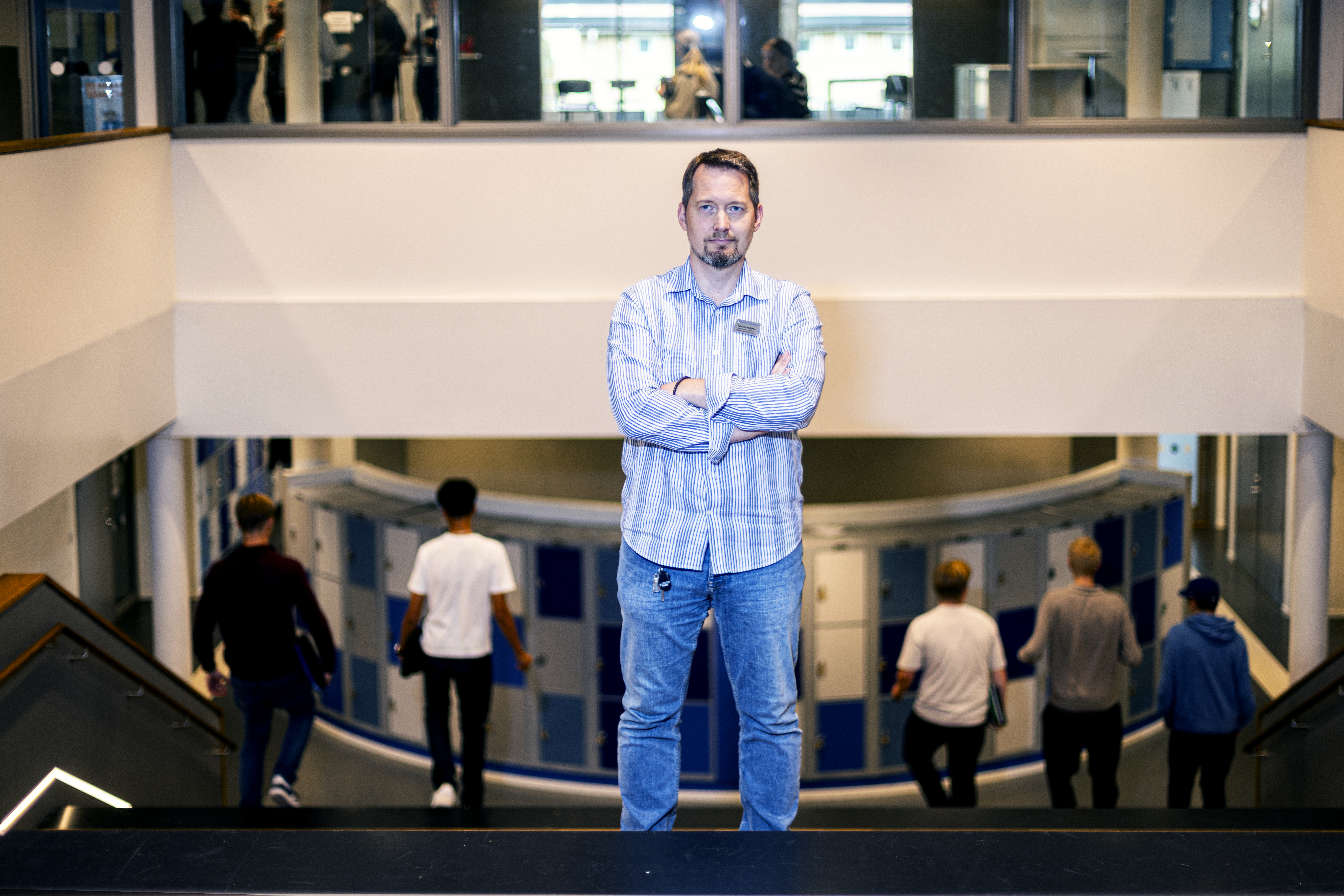 Stefan Lundgren står med armarna i kors i en trappa i en skola, inramad av elever som är på väg ned för trappan.