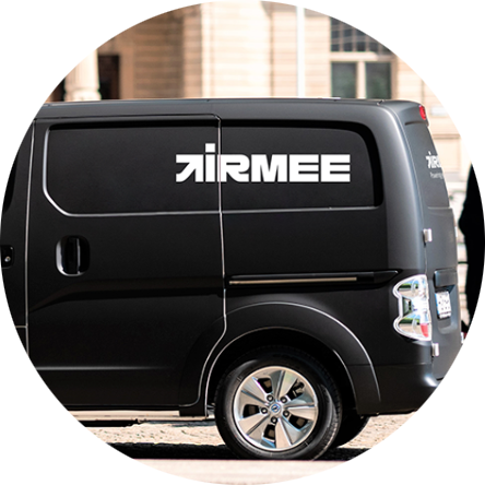 En svart skåpbil med texten "Airmee" i vita bokstäver på sidan står parkerad på en gata framför en beige byggnad.