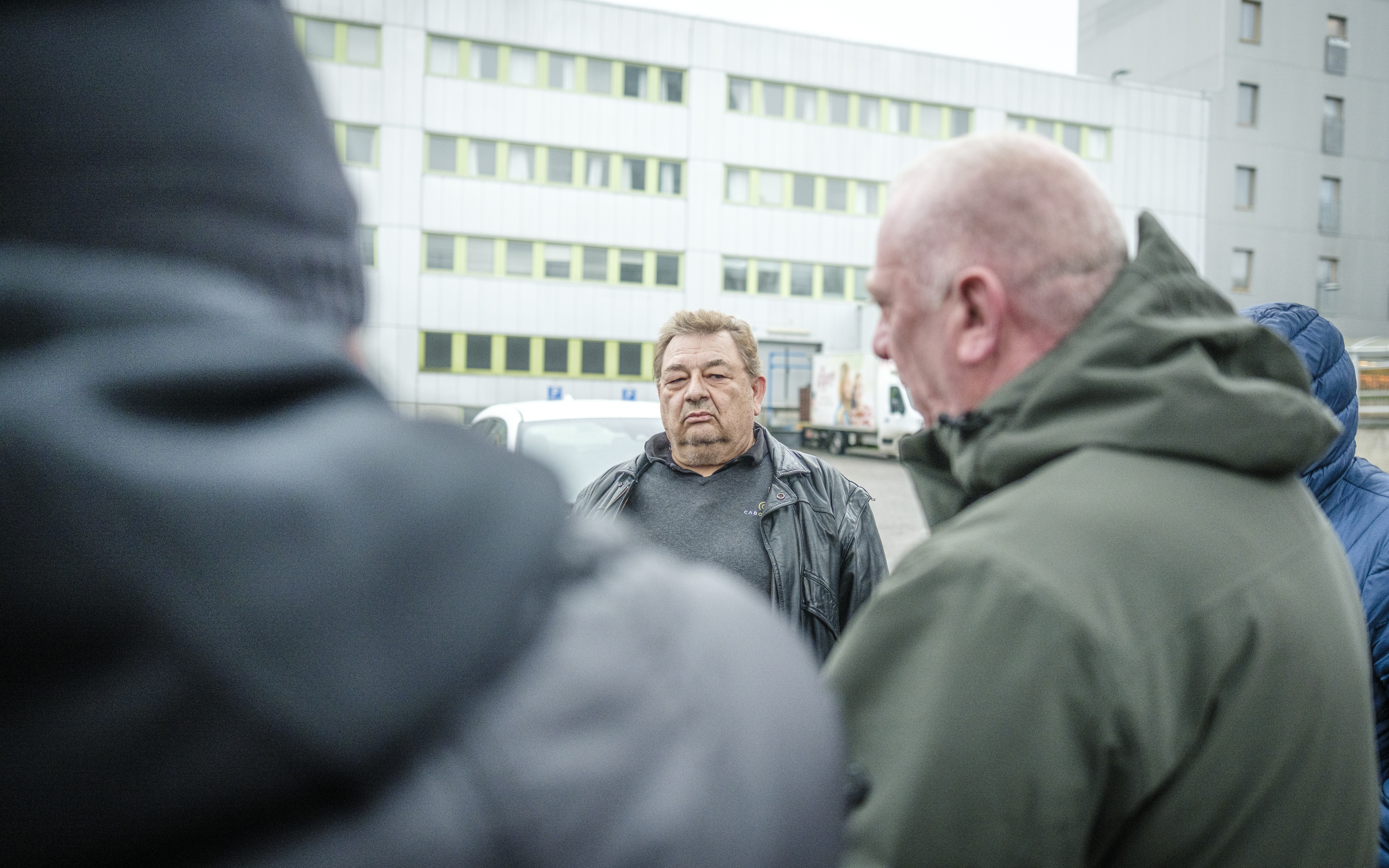 Peter Johansson i svart jacka står utomhus framför en byggnad, omgiven av andra personer med jackor.