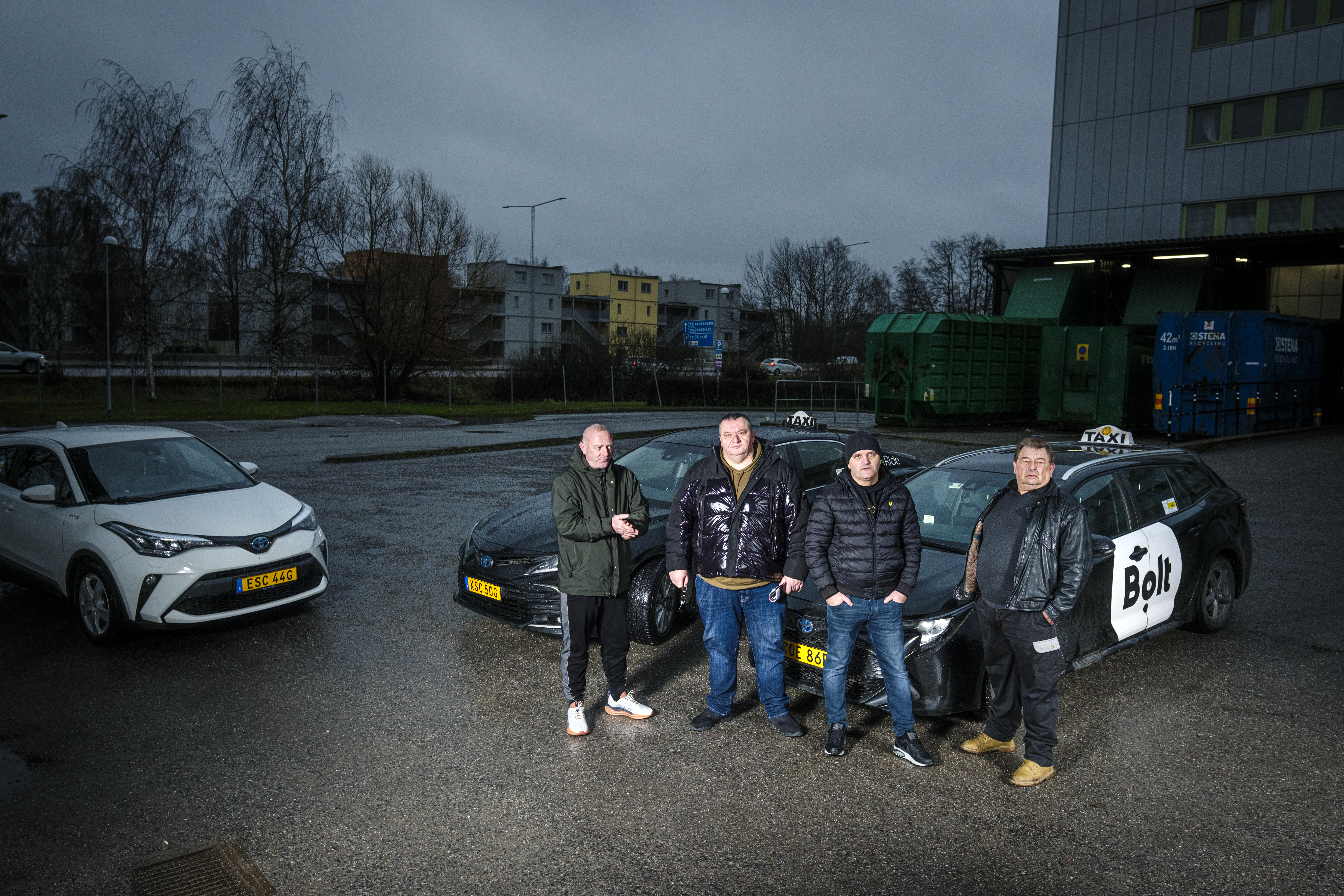 Suad Alomerovic, Enis Adrovic, Muljhan Husovic och Peter Johansson står framför två parkerade bilar, en av dem med Bolt taxiskylt, på en parkering i stadsmiljö.