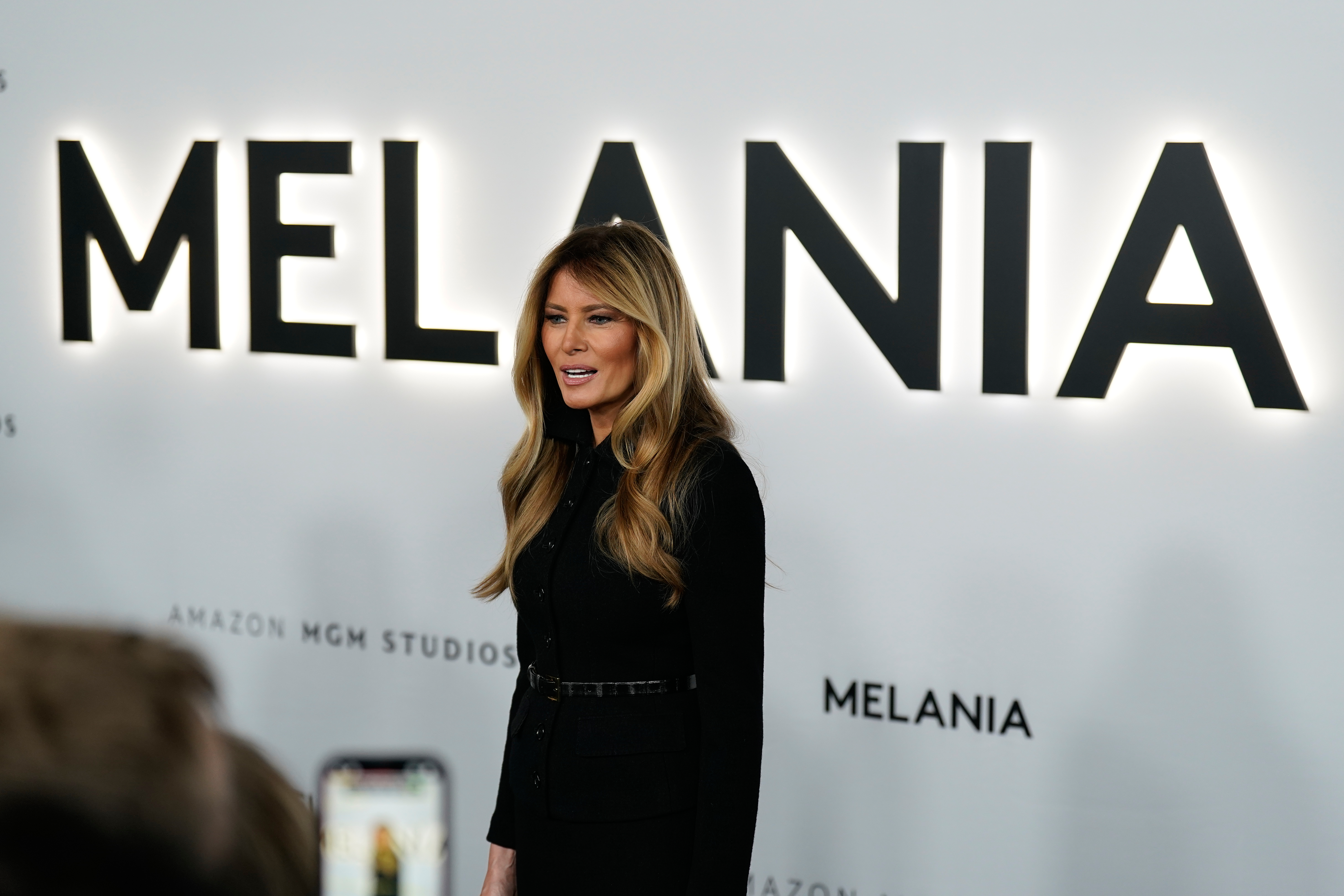 Kvinna i blont hår står framför vit bakgrund där det står Melania.