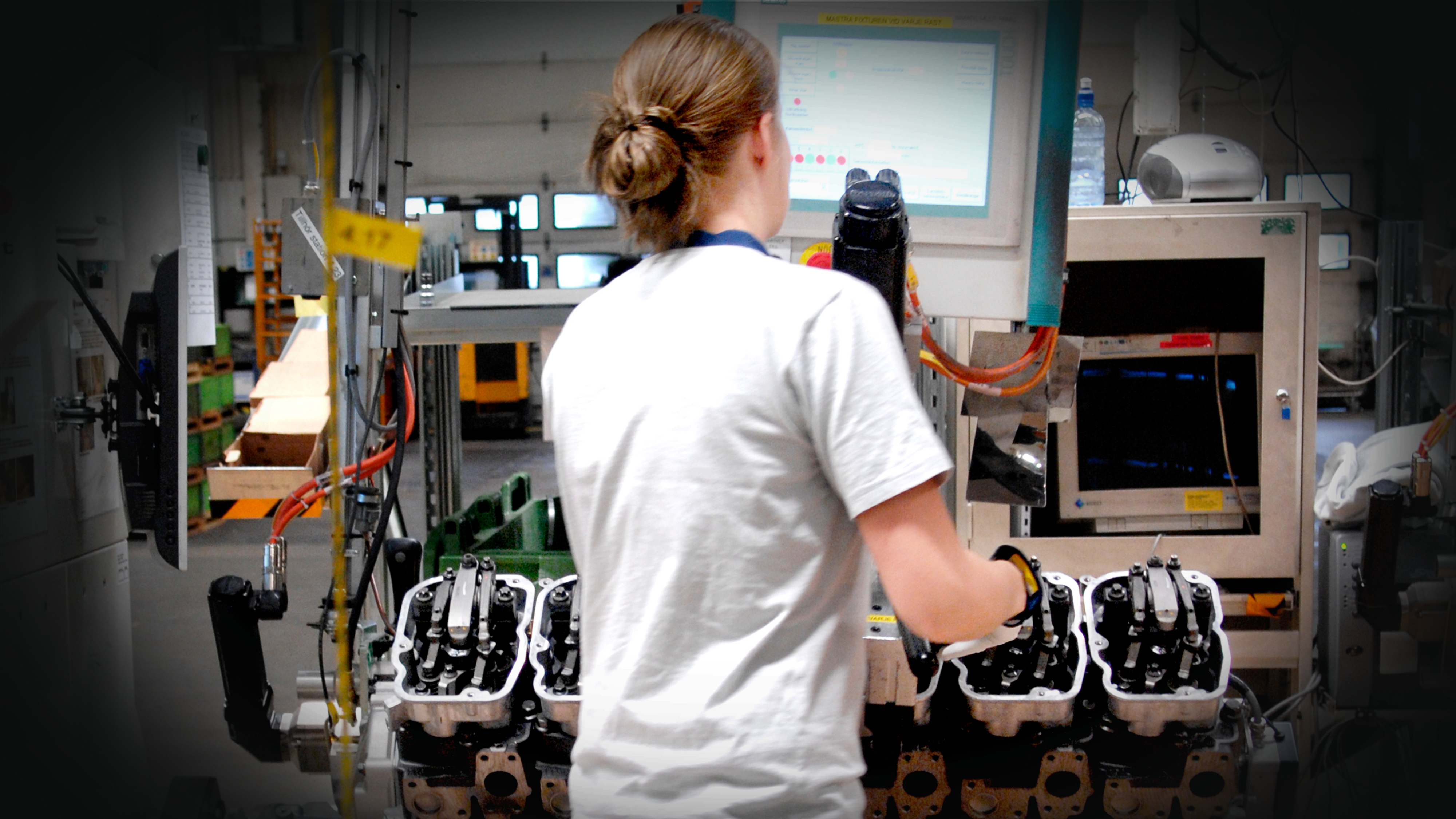 En person använder maskiner och övervakar en bildskärm vid en industriell produktionslinje för montering av motordelar.